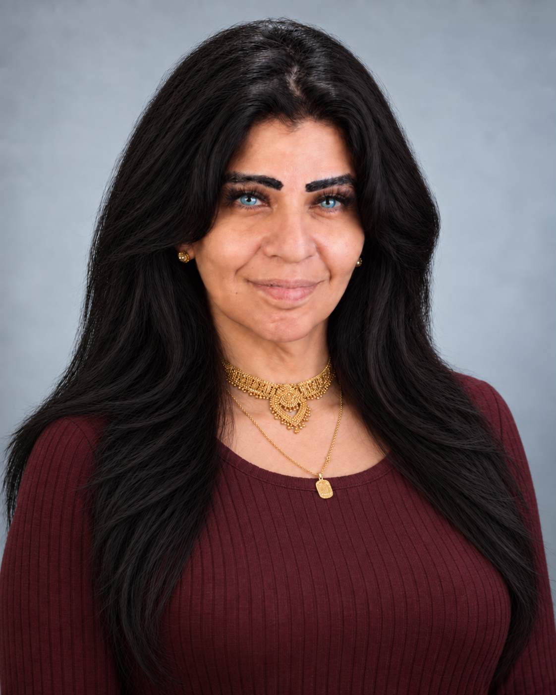Portrait of a woman with long black hair, blue eyes, wearing gold jewelry, a maroon top, and a neutral background.