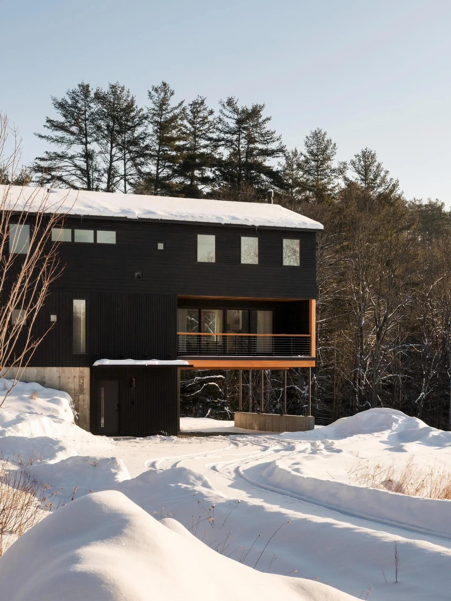 Okemo Mountain House | Set within a sloping meadow in Vermont&rsquo;s Green Mountains, the house spans its terrain rather than cutting into it. A single volume rests on slender steel posts anchored to a concrete retaining wall, allowing the meadow to