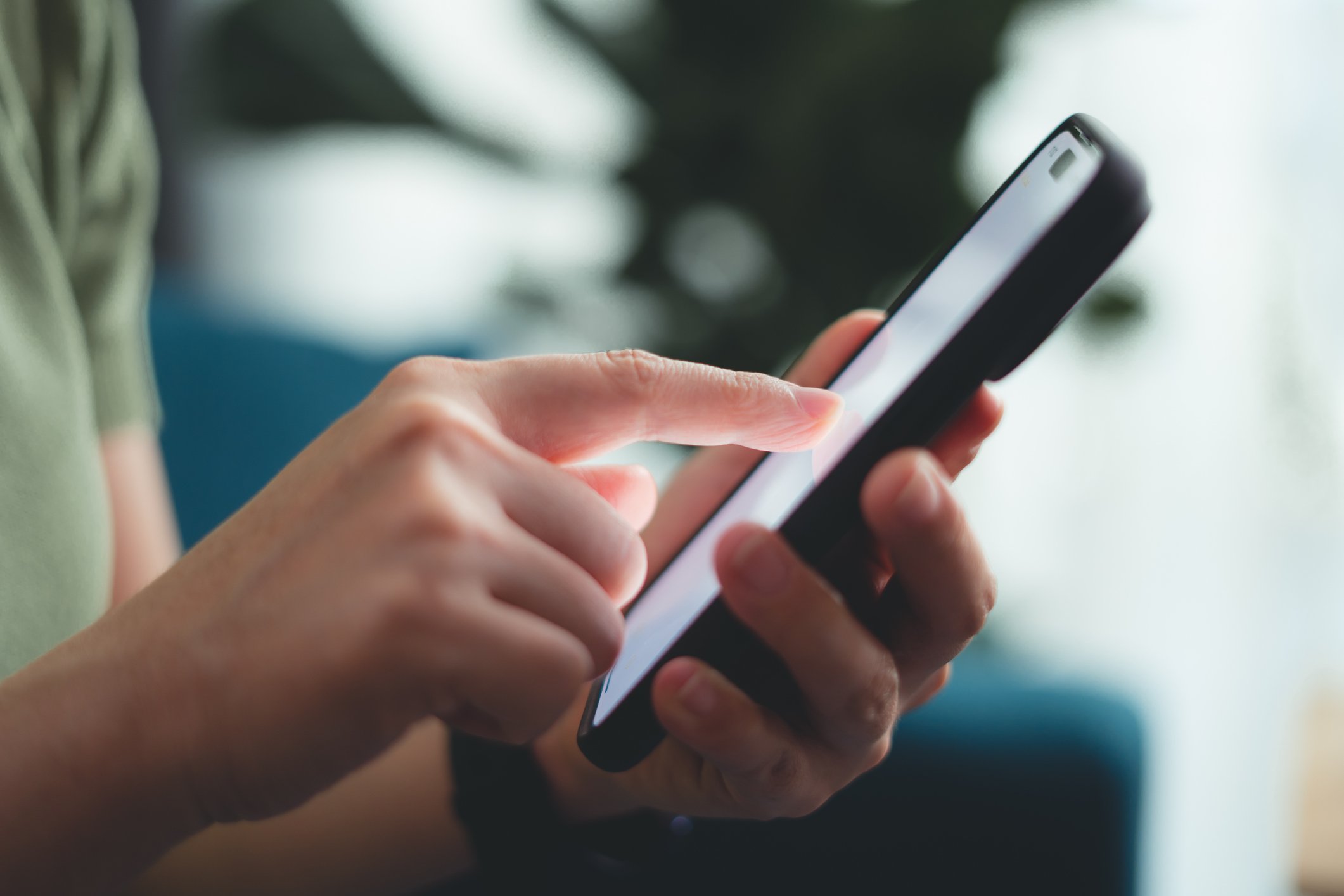 Close-up of a person's hand holding and using a smartphone with a blurred background.