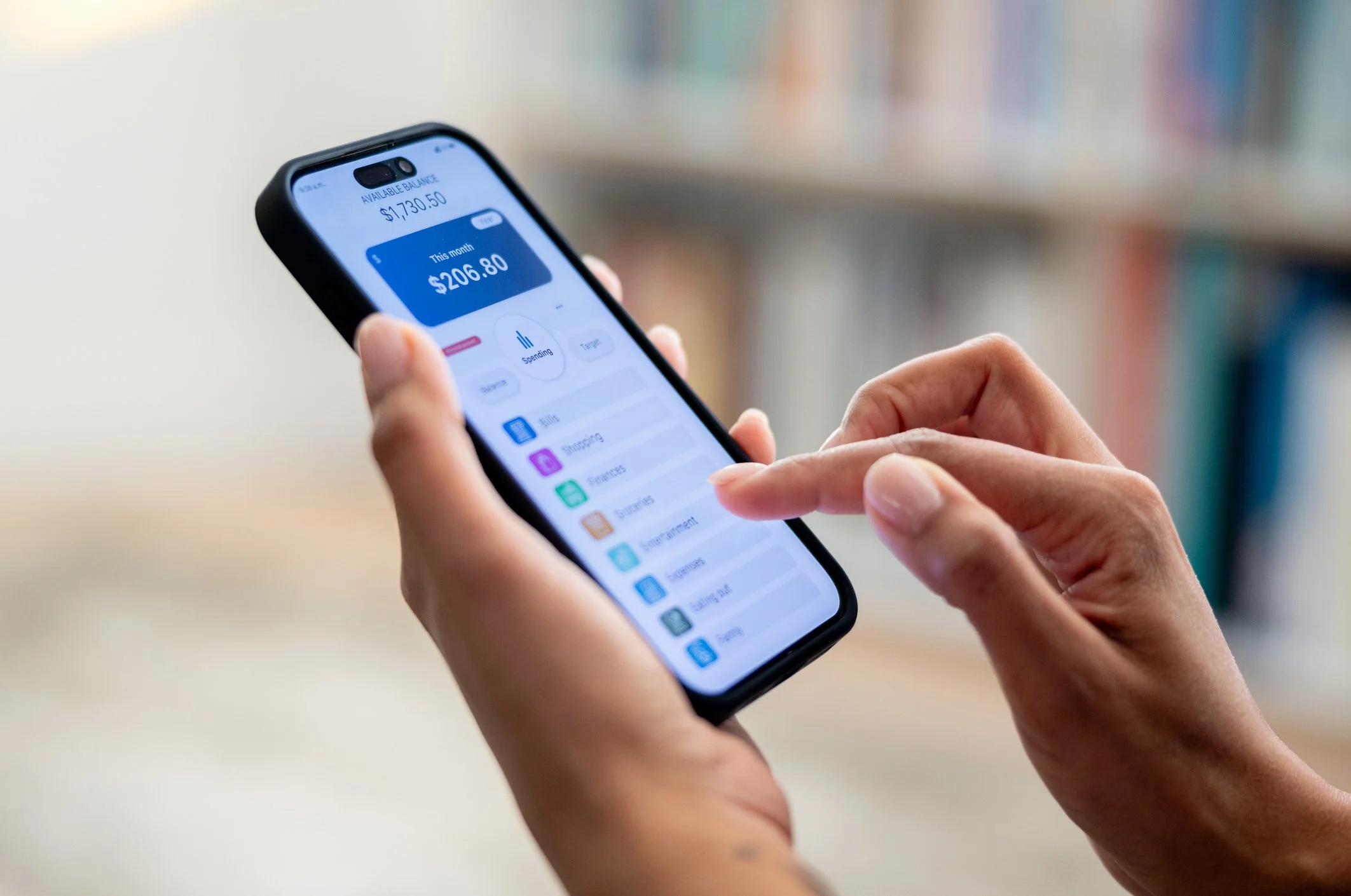 Close-up of a person's hands holding a smartphone displaying a financial app with an available balance of $1,730.50 and spending of $206.80.