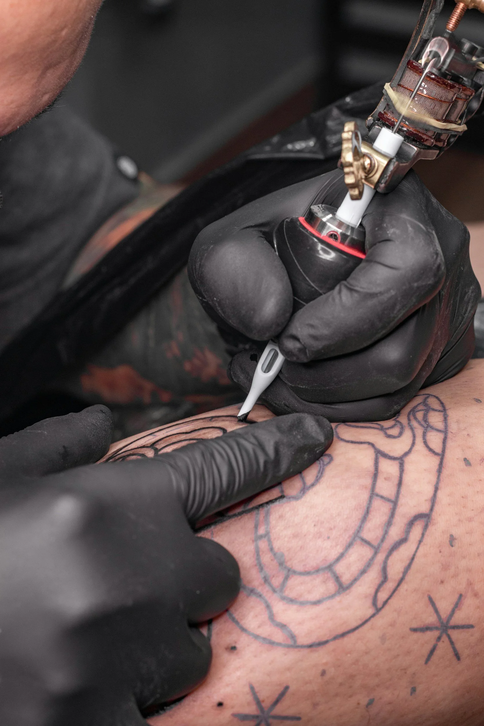 A person with a tattoo on their arm getting a tattoo done by an artist wearing black gloves.