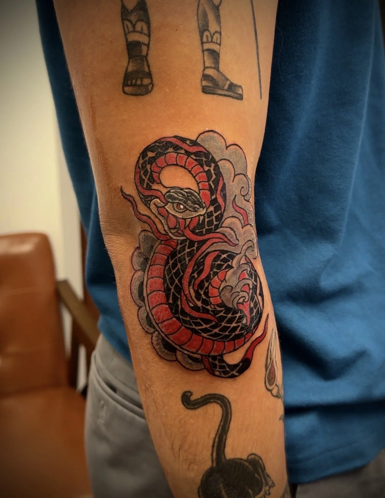 Tattoo of a black and red snake wrapped around a cloud on a person's forearm.