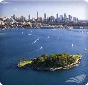 Aerial view of downtown skyline over a bay with a small island in the foreground and several sailboats on the water.