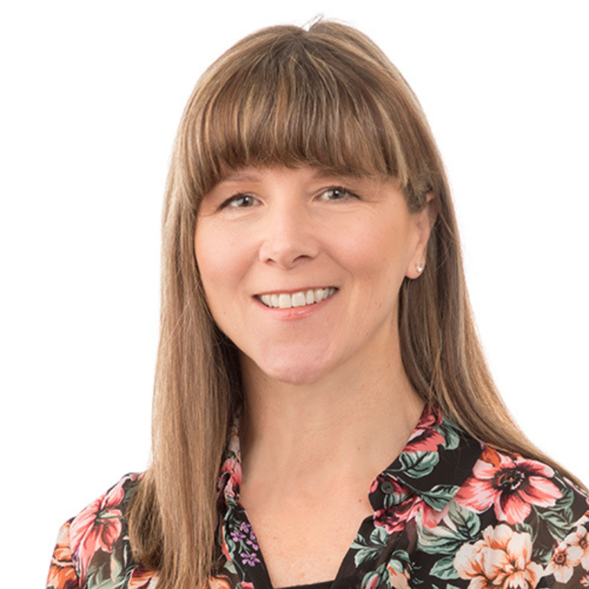 A woman with long, light brown hair and a fringe, smiling, wearing a black floral blouse against a white background.