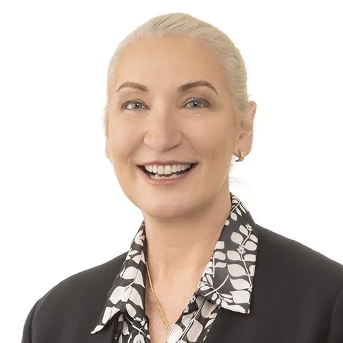 Lainey Murphey. A smiling woman with platinum blonde hair styled in a bun, wearing a black blazer over a patterned blouse, against a plain white background.