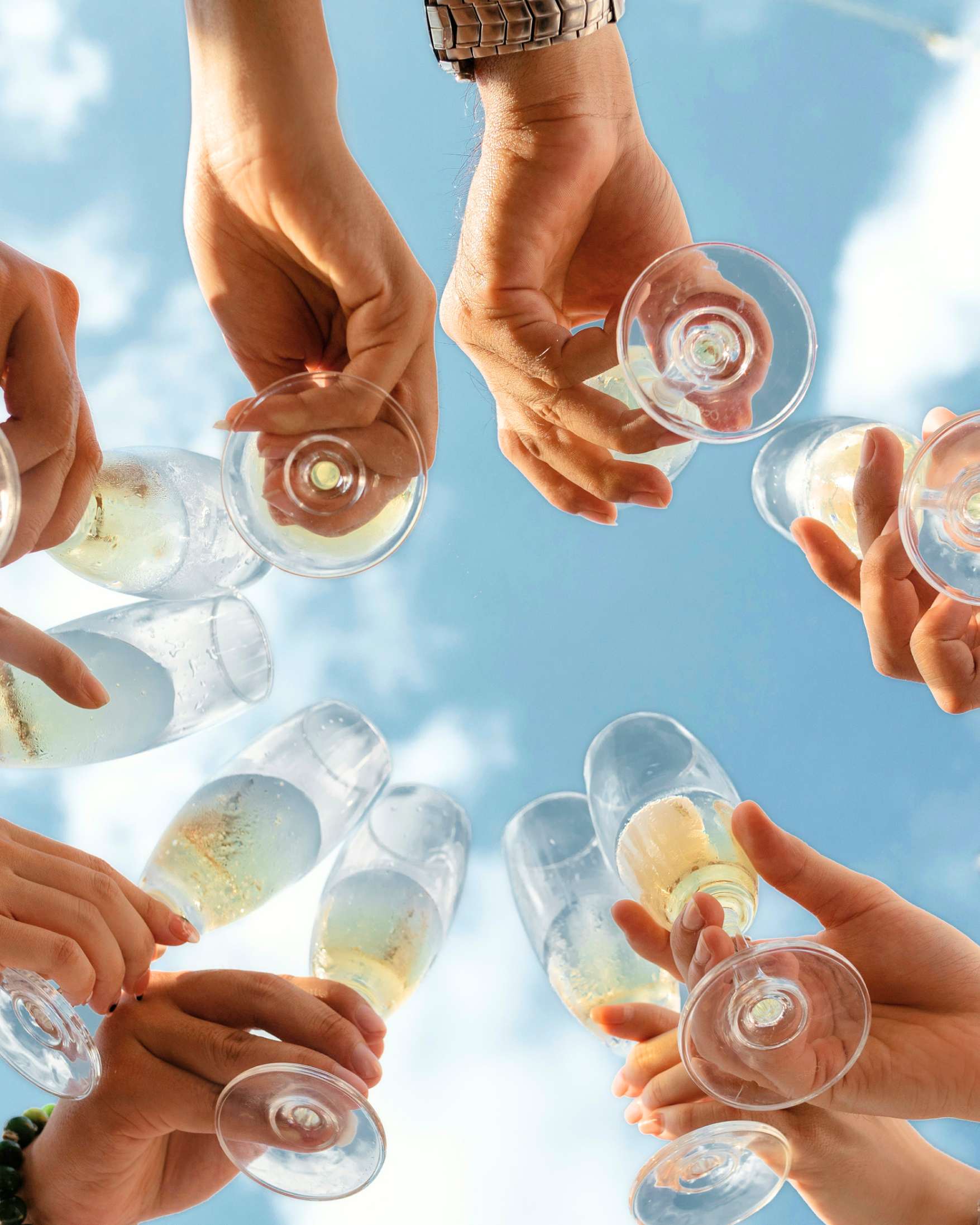 People toasting with champagne glasses against a blue sky.