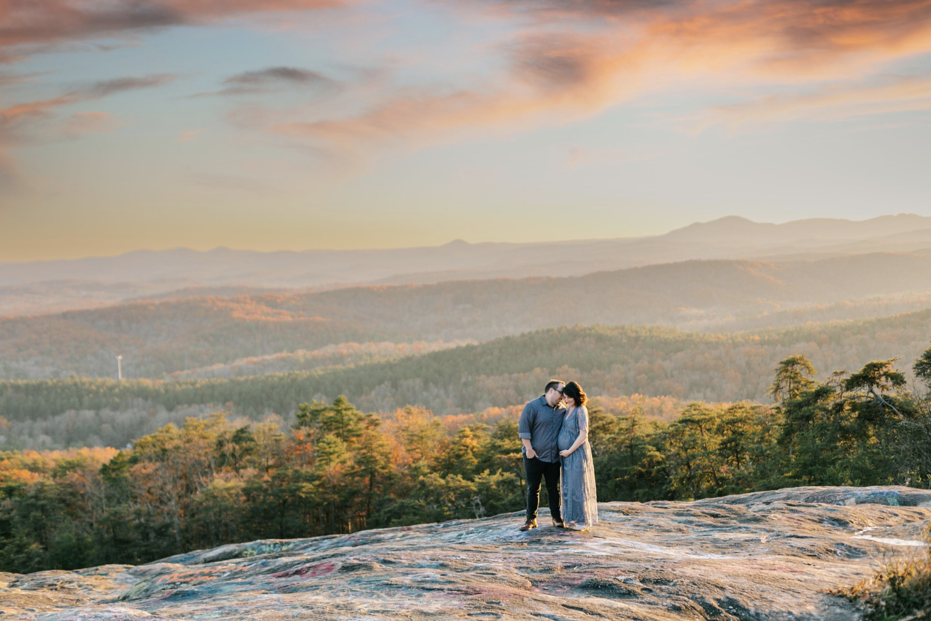 A couple embracing on a scenic overlook with a vast landscape at sunset.
