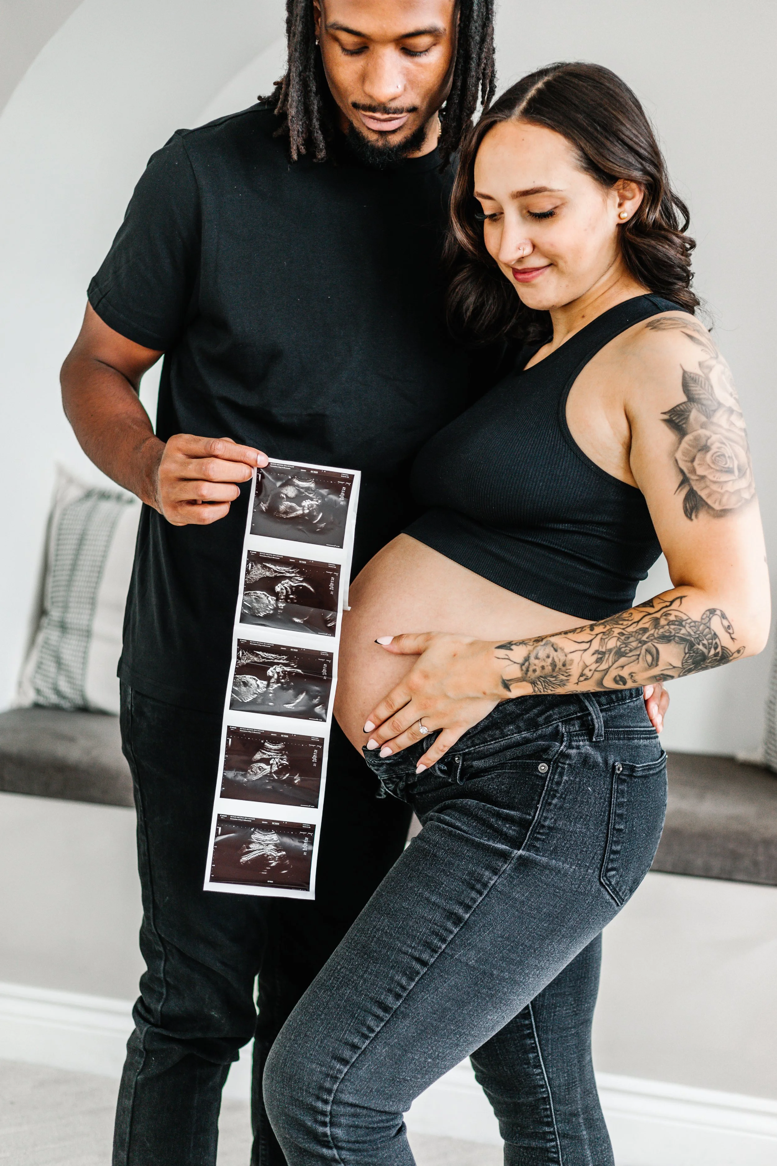 Pregnant couple holding ultrasound photos, woman cradling baby bump.