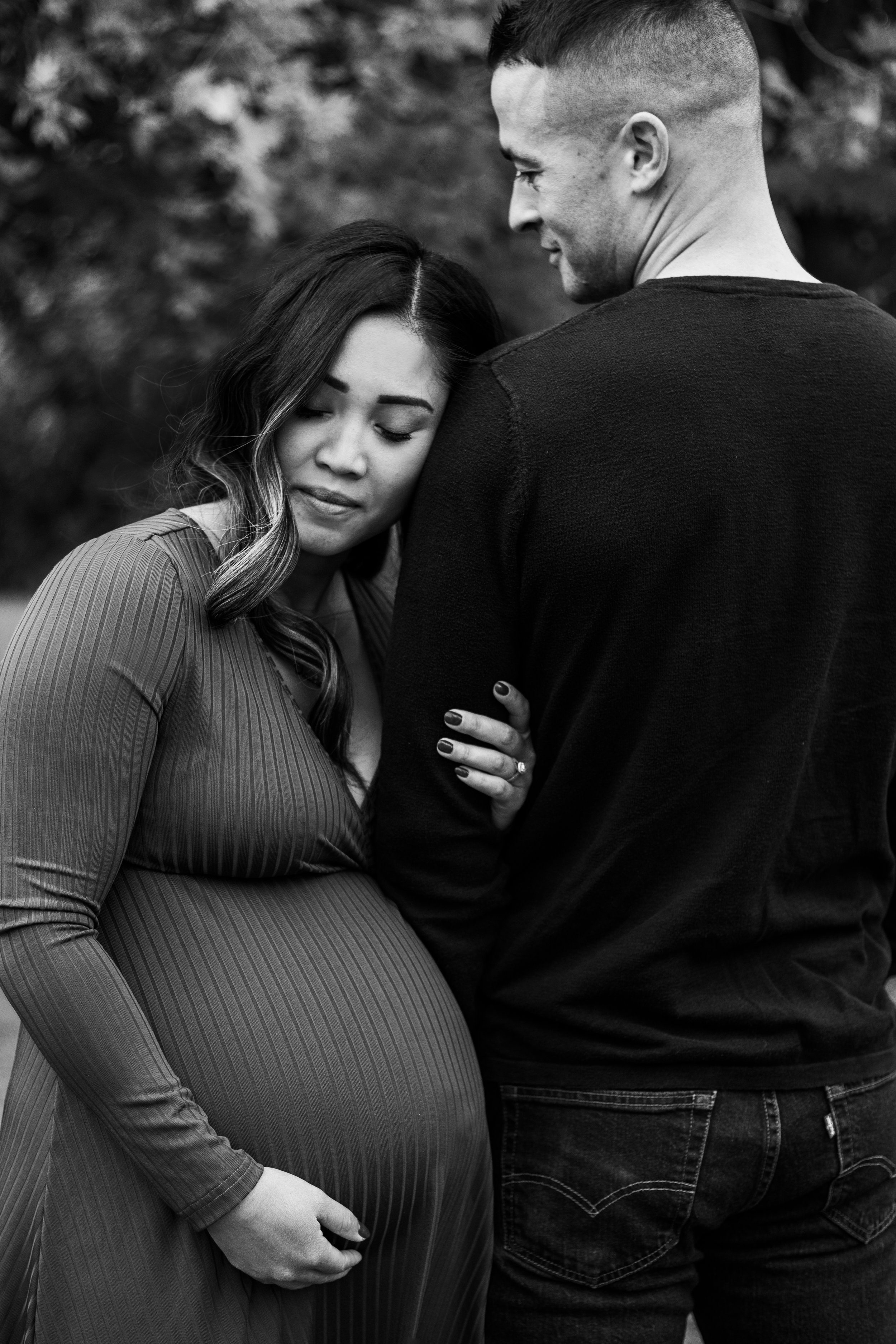 Black and white photo of a pregnant woman leaning on a man's back, her hand on her belly.