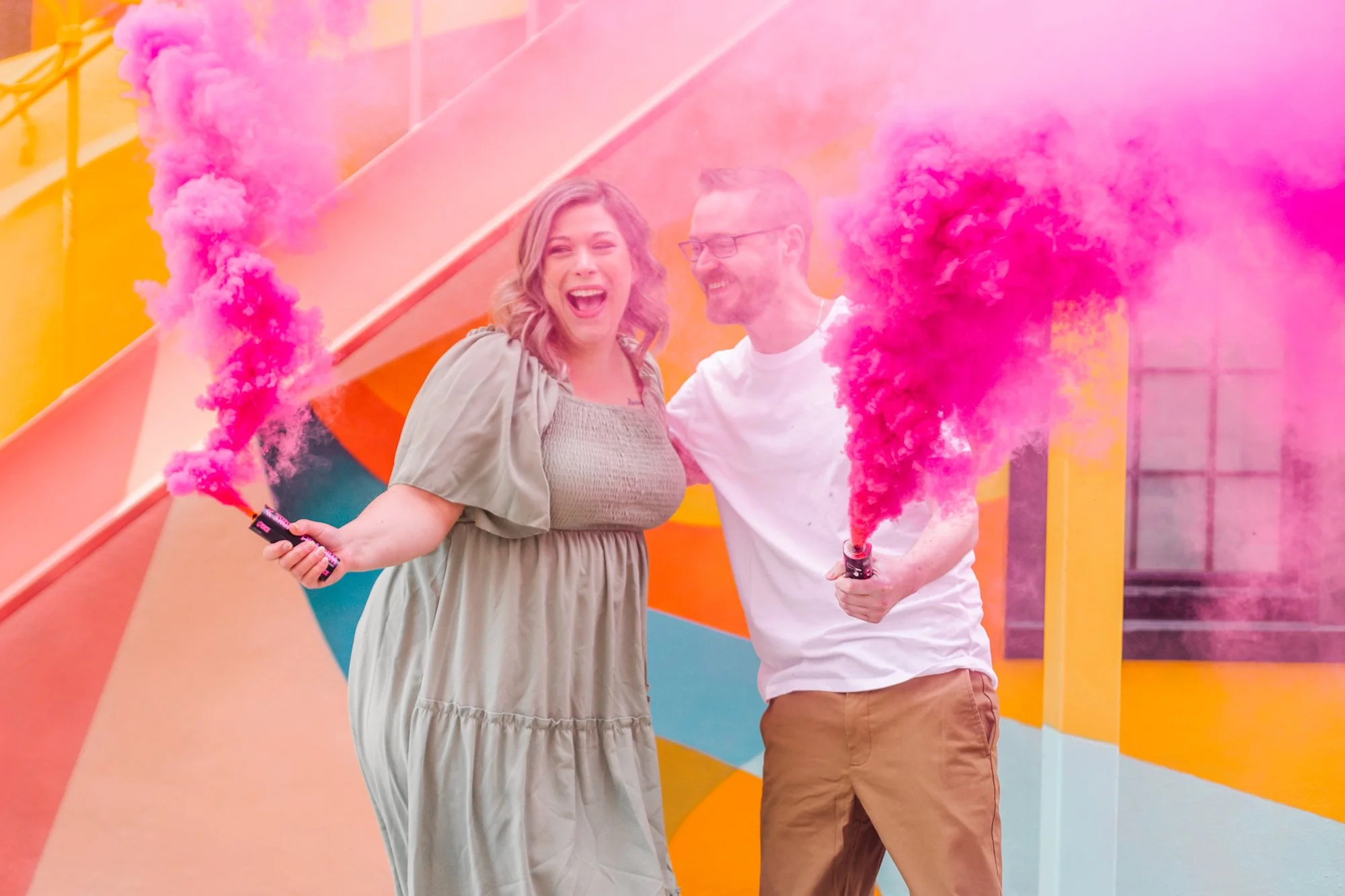 Couple celebrating with pink smoke bombs in front of colorful backdrop