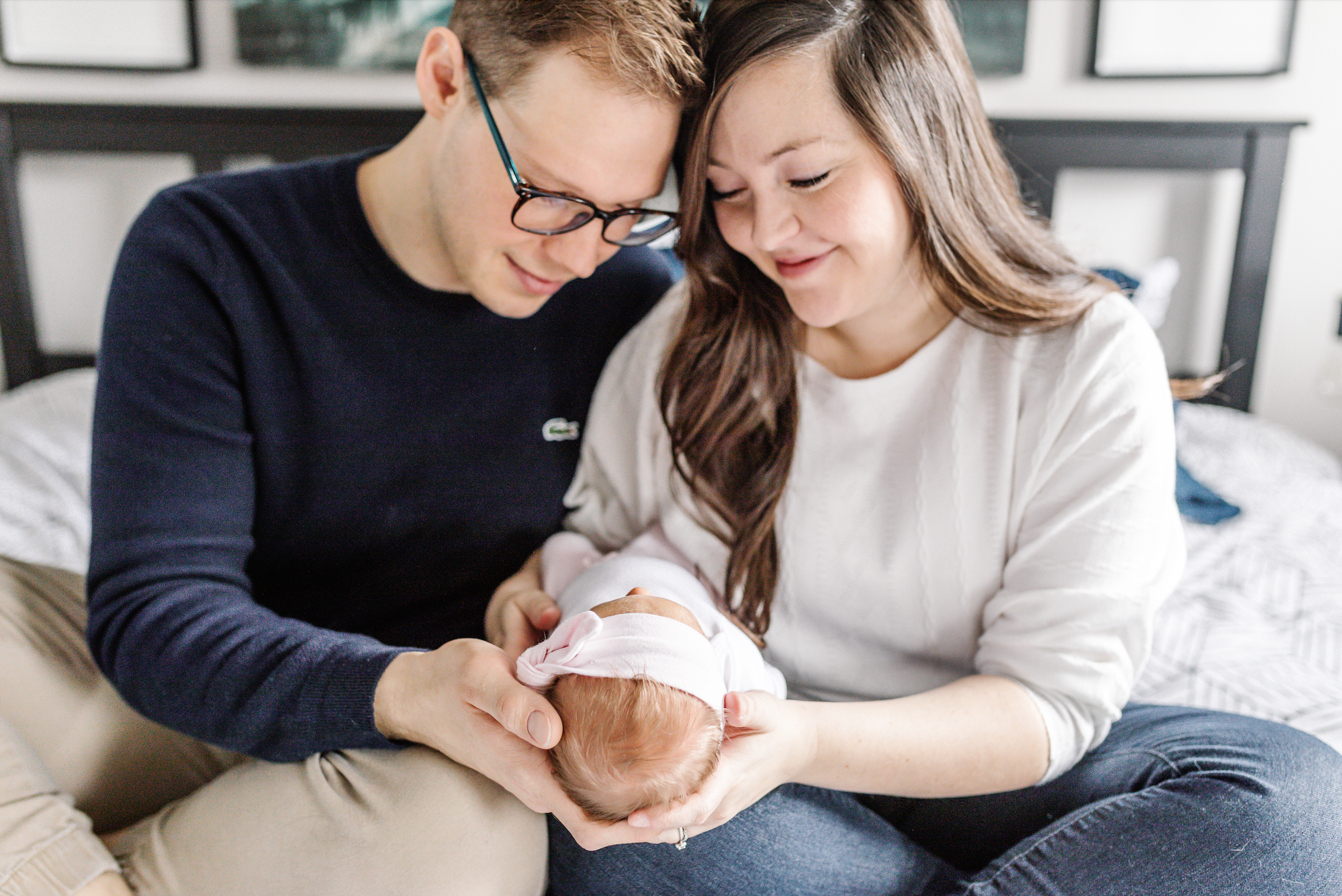A couple lovingly cradling their newborn baby while sitting on a bed.
