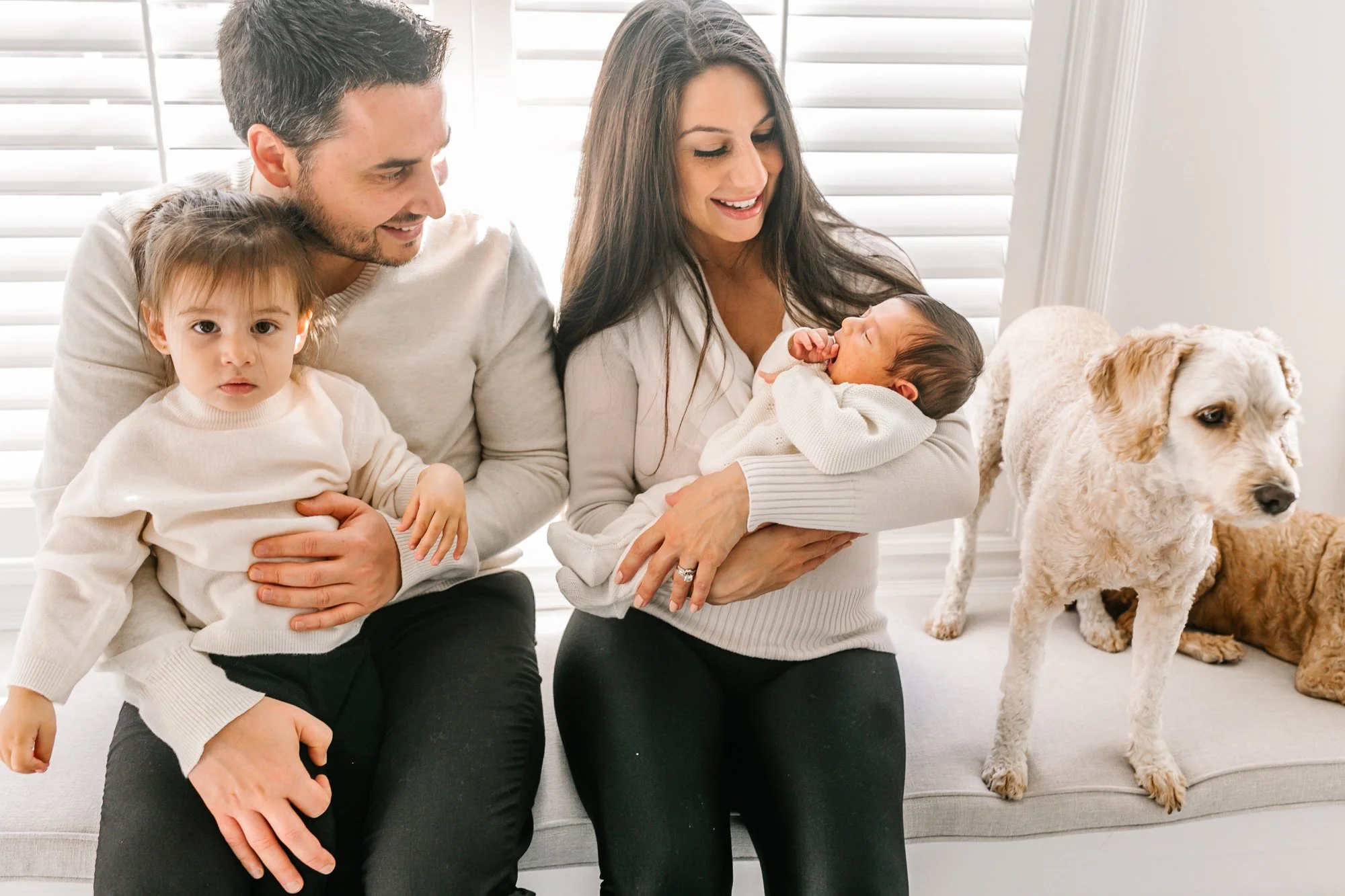 Family with two children and a dog sitting indoors on a bench.