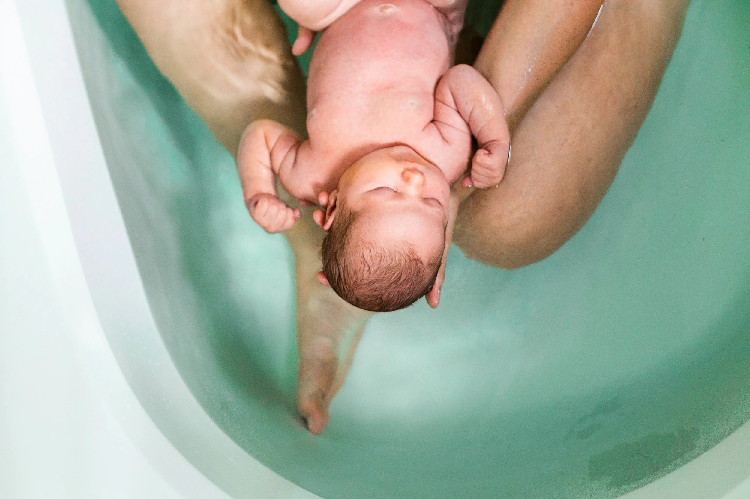 Newborn baby being held in a bathtub