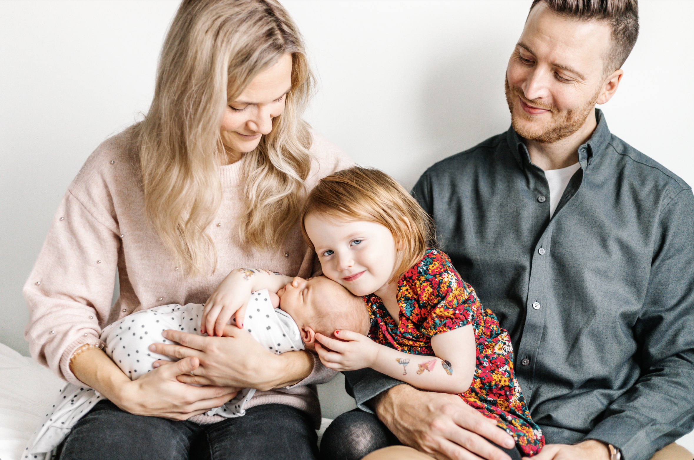 Family with mother holding newborn, child hugging baby, and father smiling.