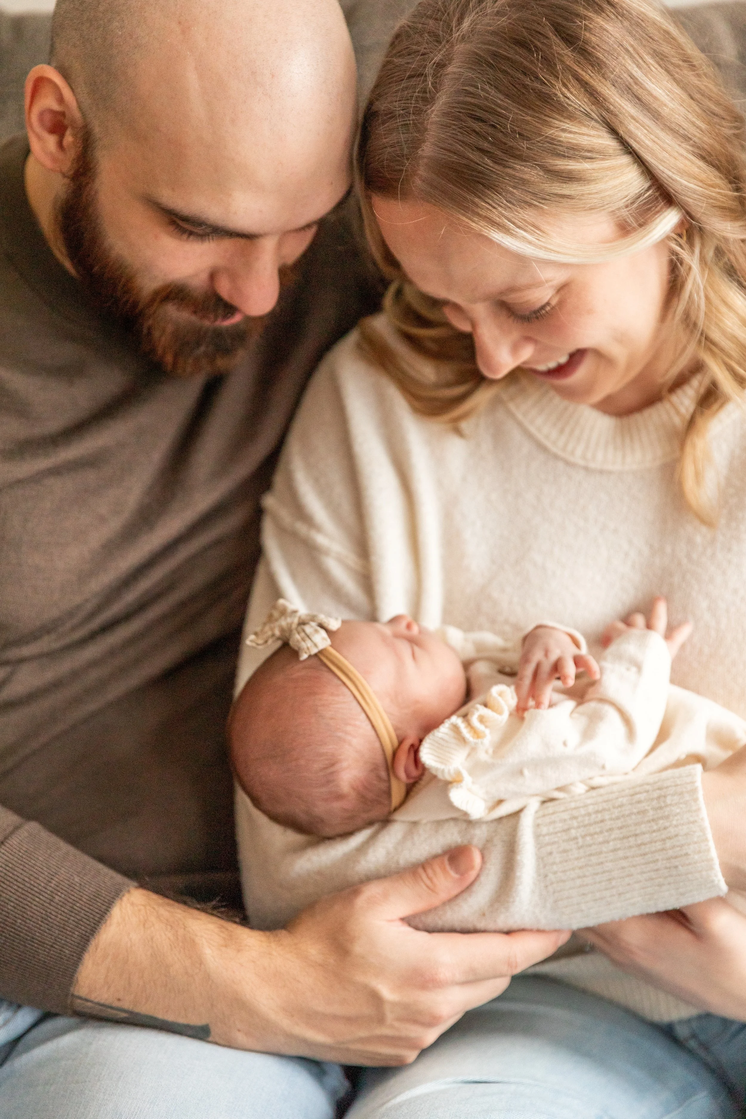 A couple holding a newborn baby, smiling and looking at the baby, with the woman sitting on the man's lap.