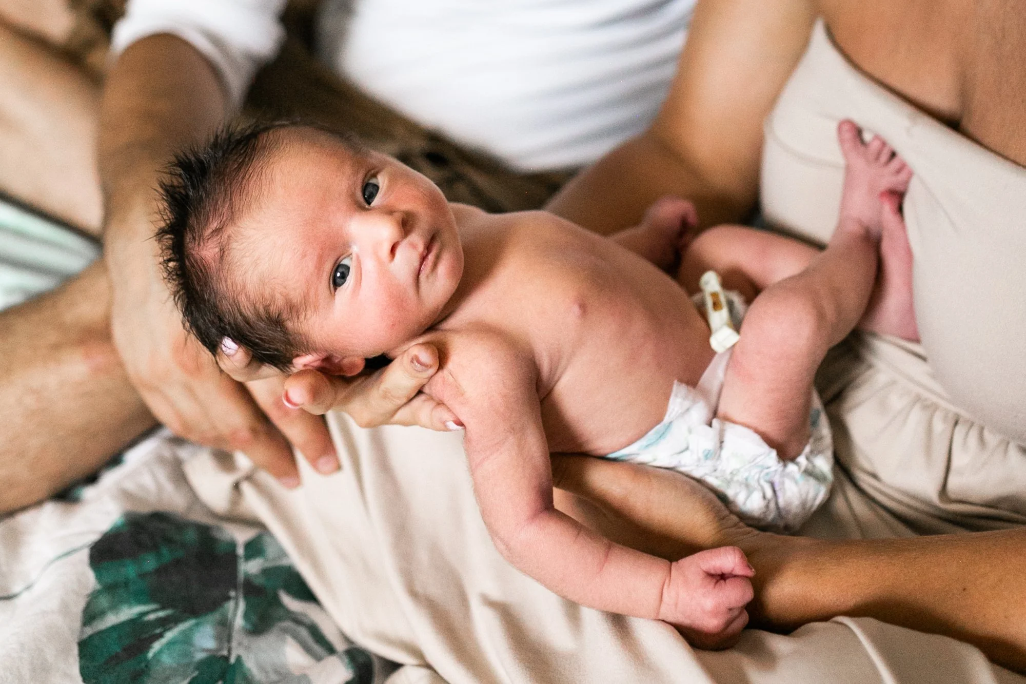 Newborn baby lying on an adult's lap, wearing a diaper.
