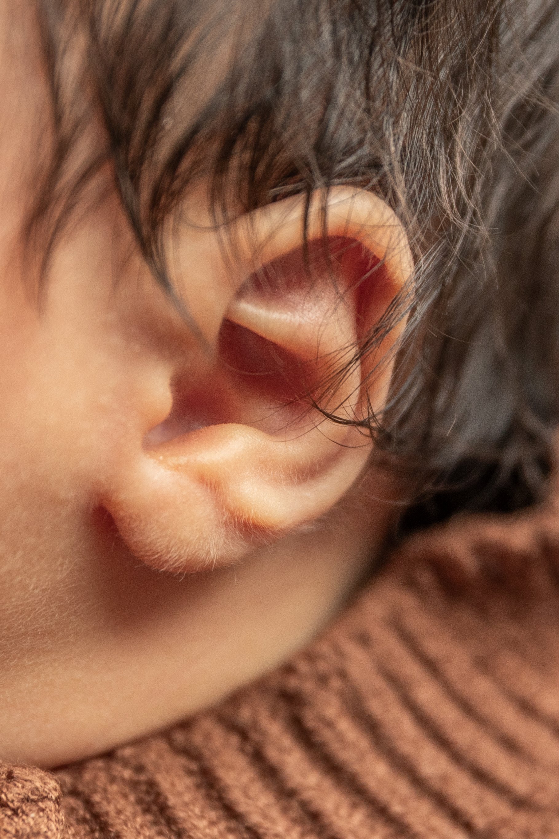 Close-up of a person's ear with dark hair and a brown knitted fabric underneath.