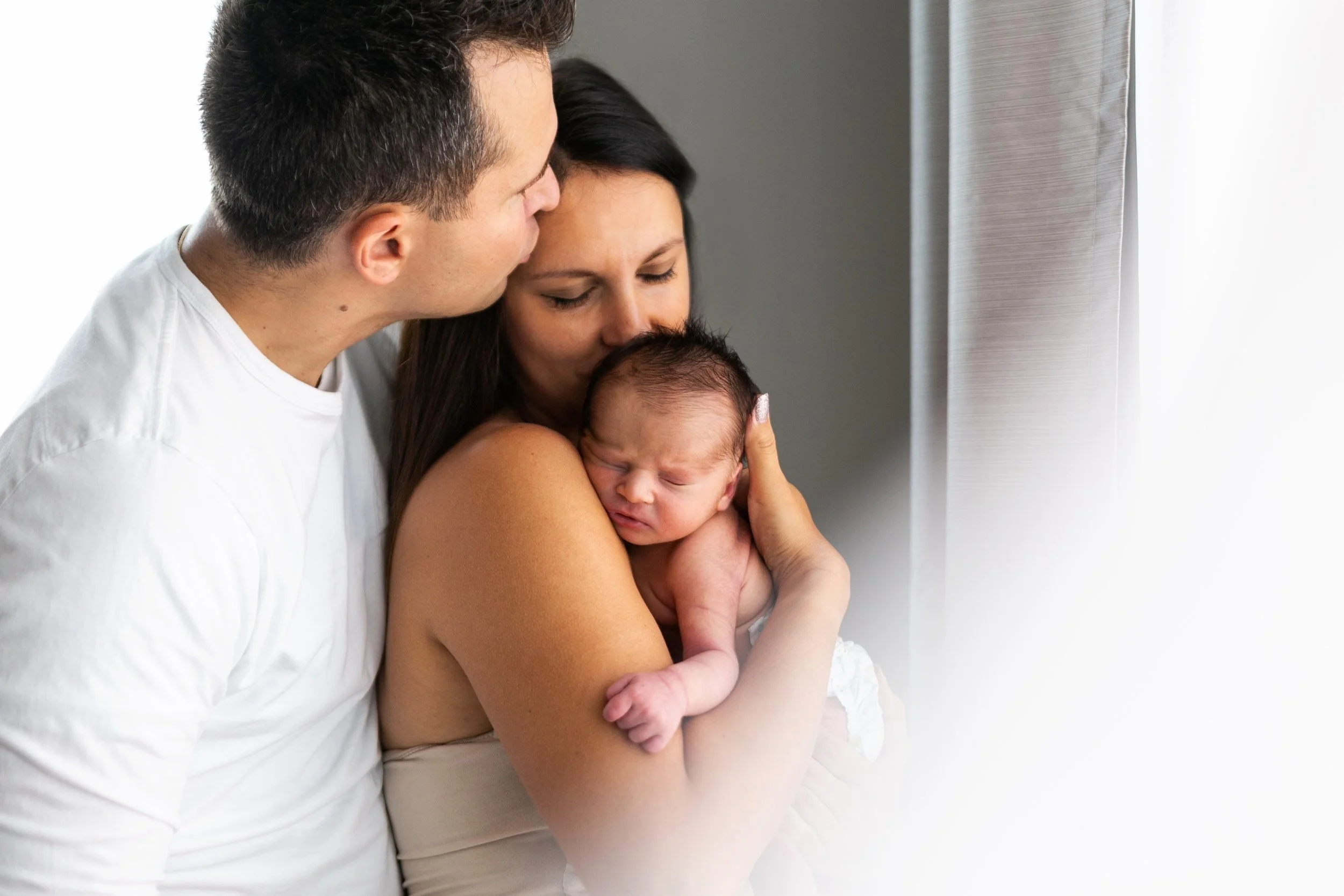 Parents holding and snuggling a newborn baby in a tender embrace.