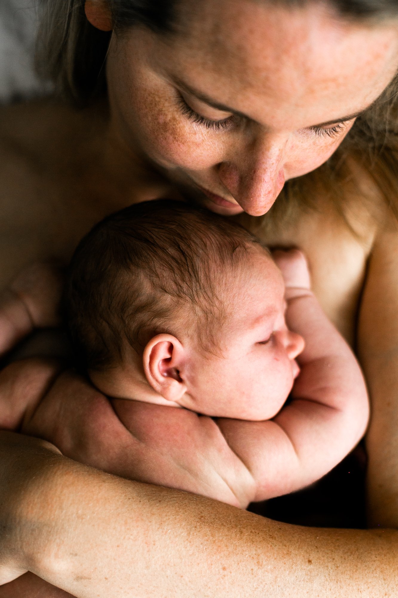 A mother holding and cuddling her sleeping newborn baby.
