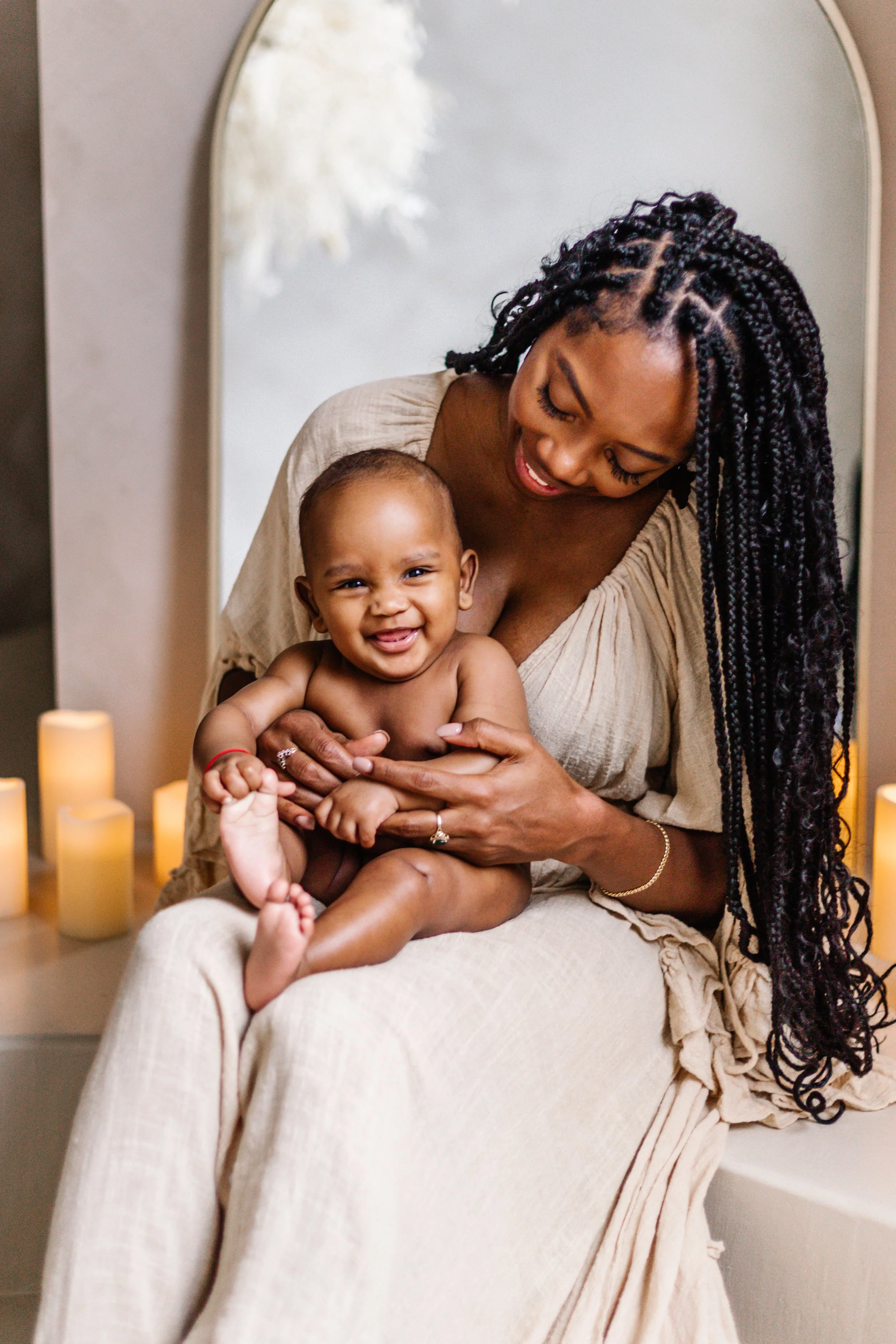 Smiling woman holding a happy baby, surrounded by lit candles in a cozy setting.