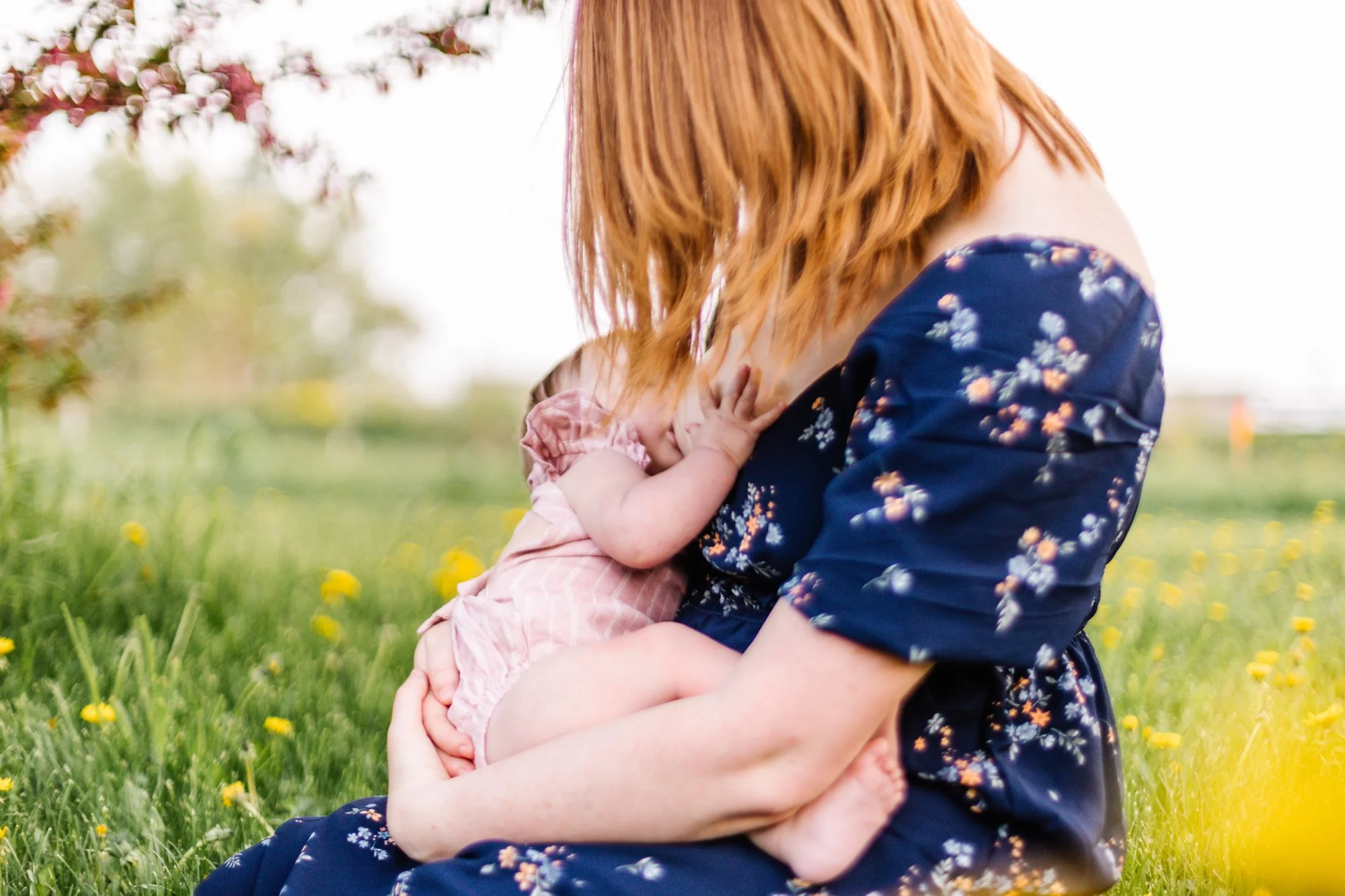Mother breastfeeding baby in a grassy field with wildflowers.