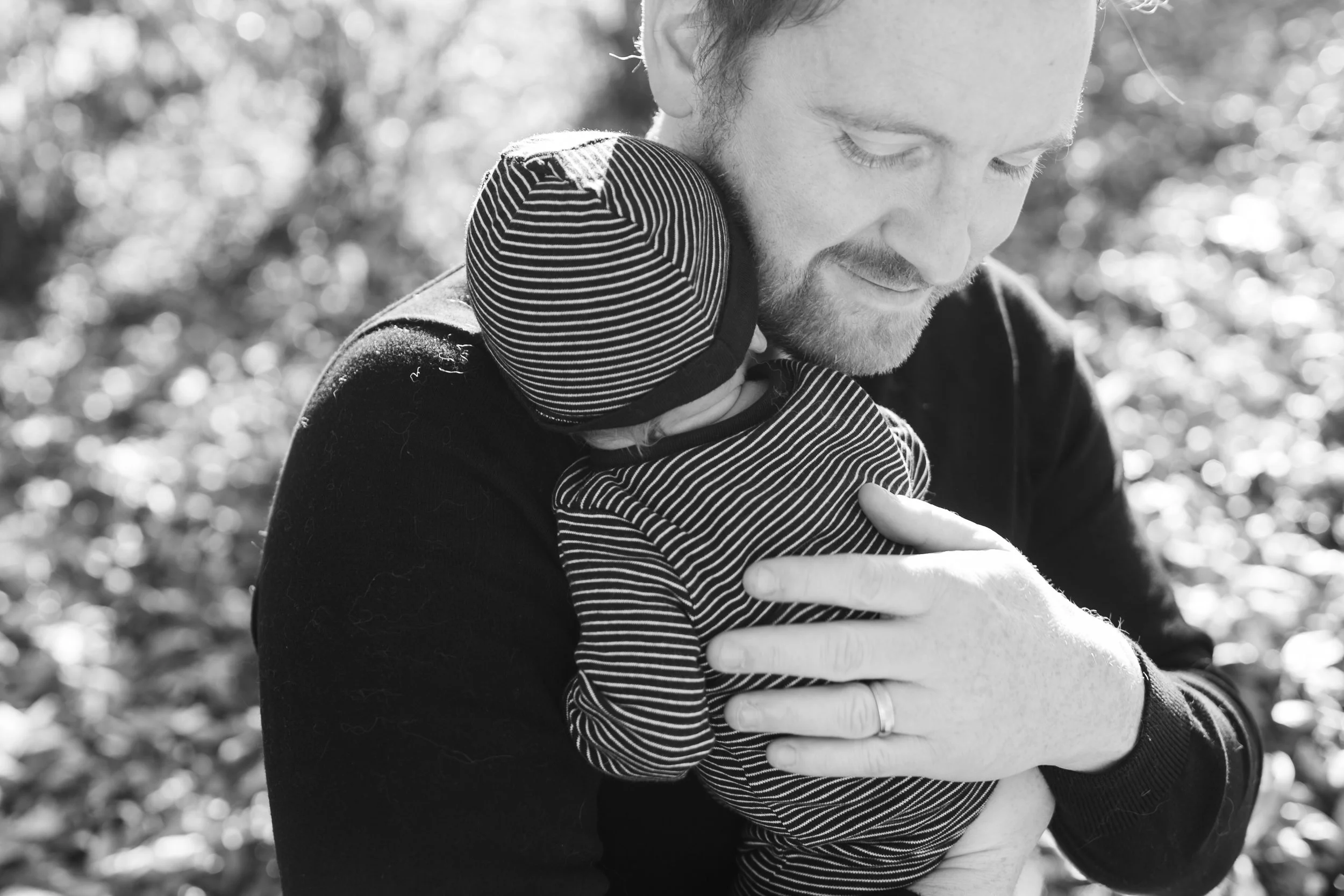 Black and white photo of a man holding a baby dressed in matching striped clothing outdoors.