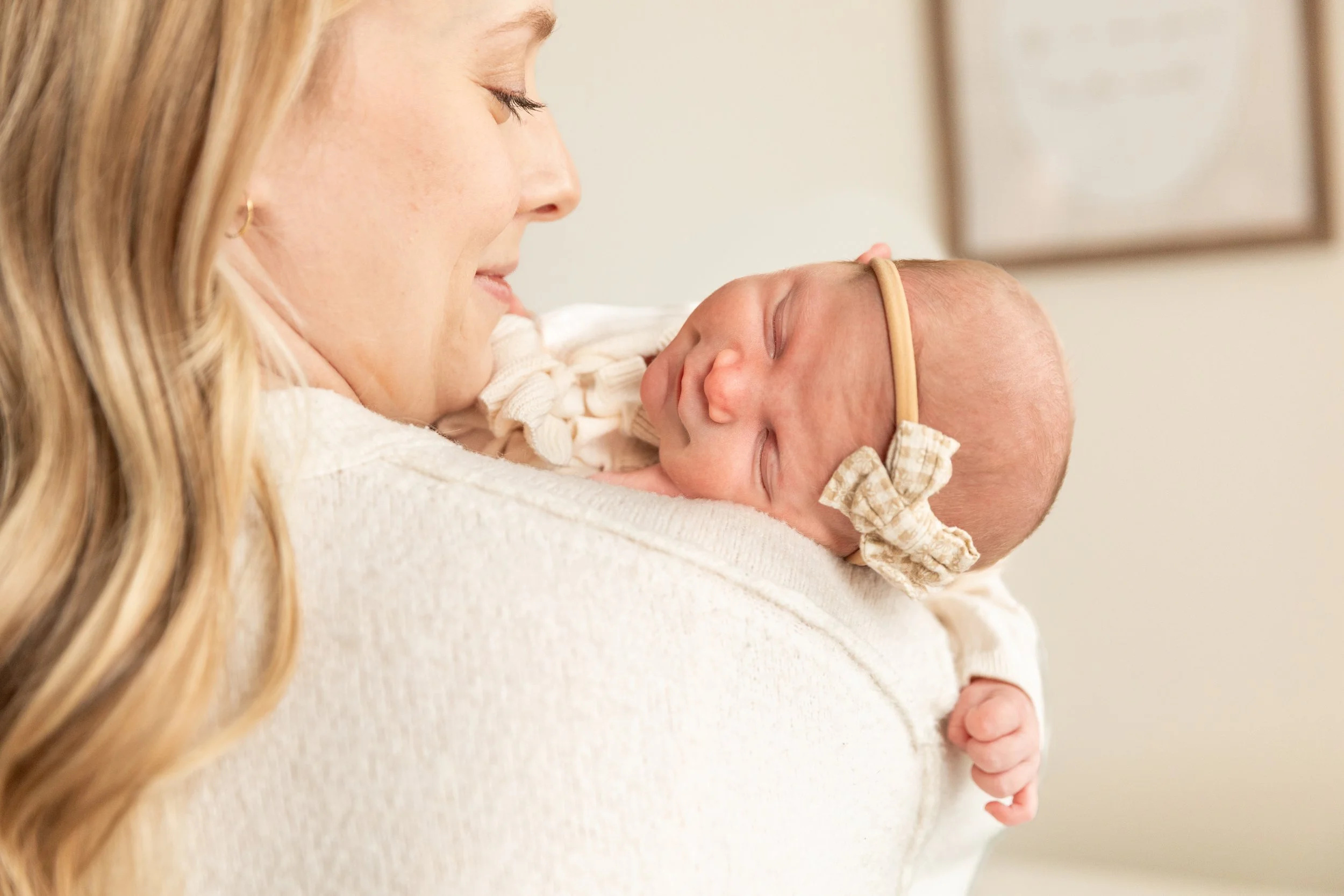 Close-up of a woman holding a sleeping baby, both smiling softly, with the woman looking at the baby.