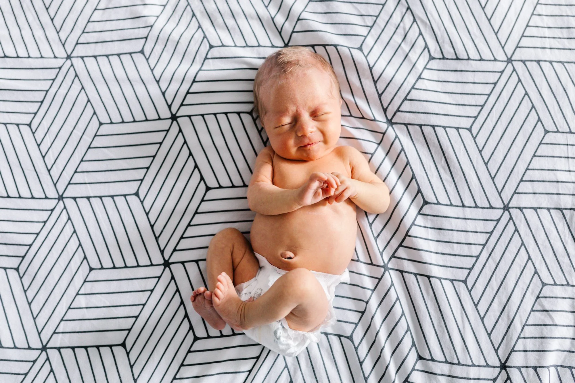 Newborn baby lying on geometric patterned blanket.