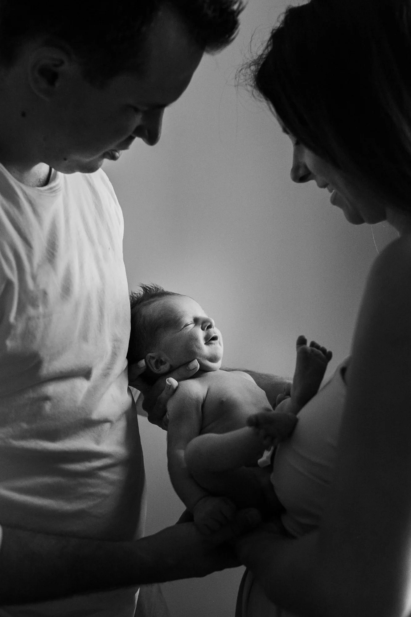 Black and white photo of a couple holding a newborn baby, smiling and looking at the child.