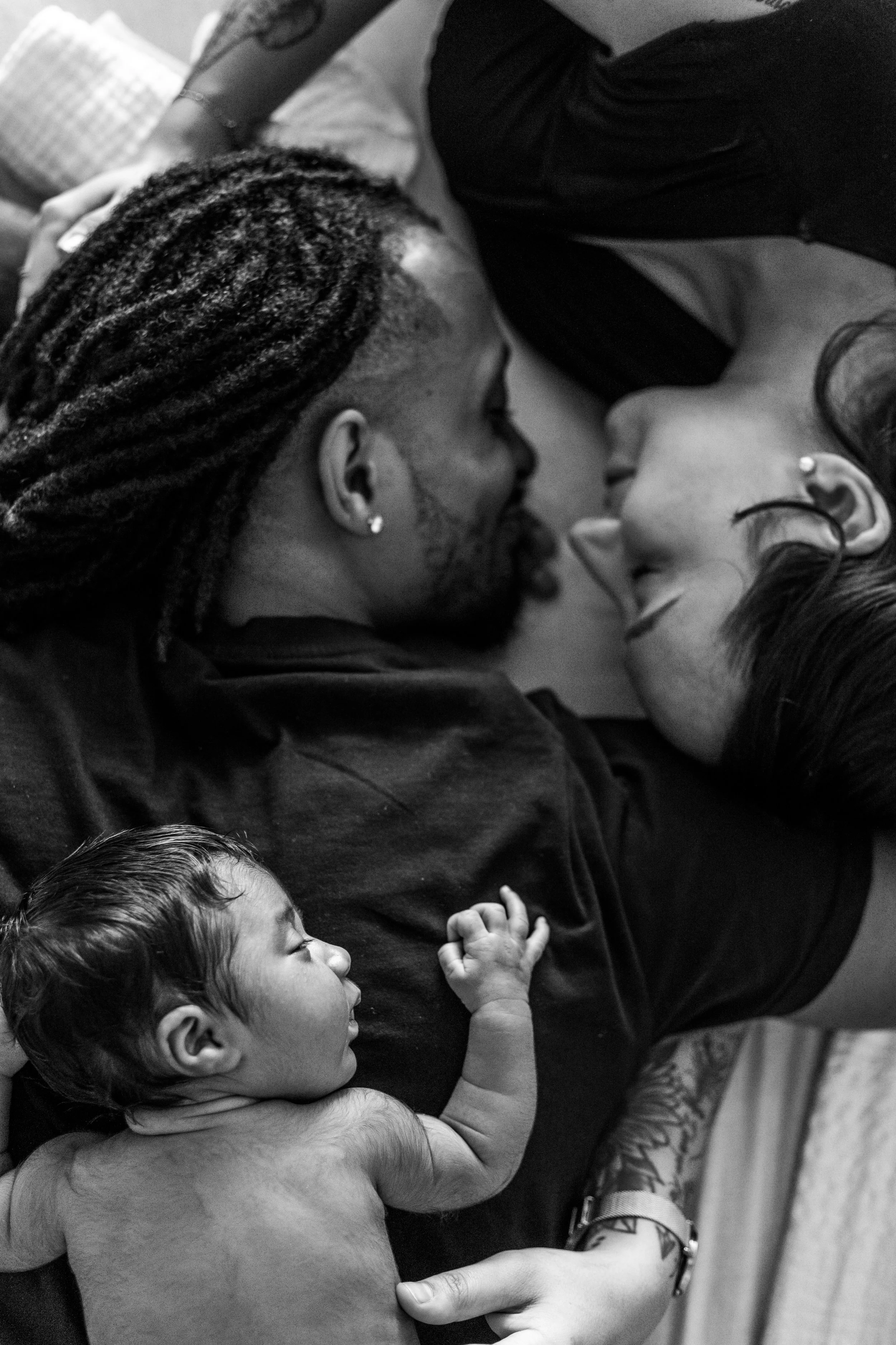 Black and white photo of a couple lying on a bed with a newborn baby resting on the man's chest.