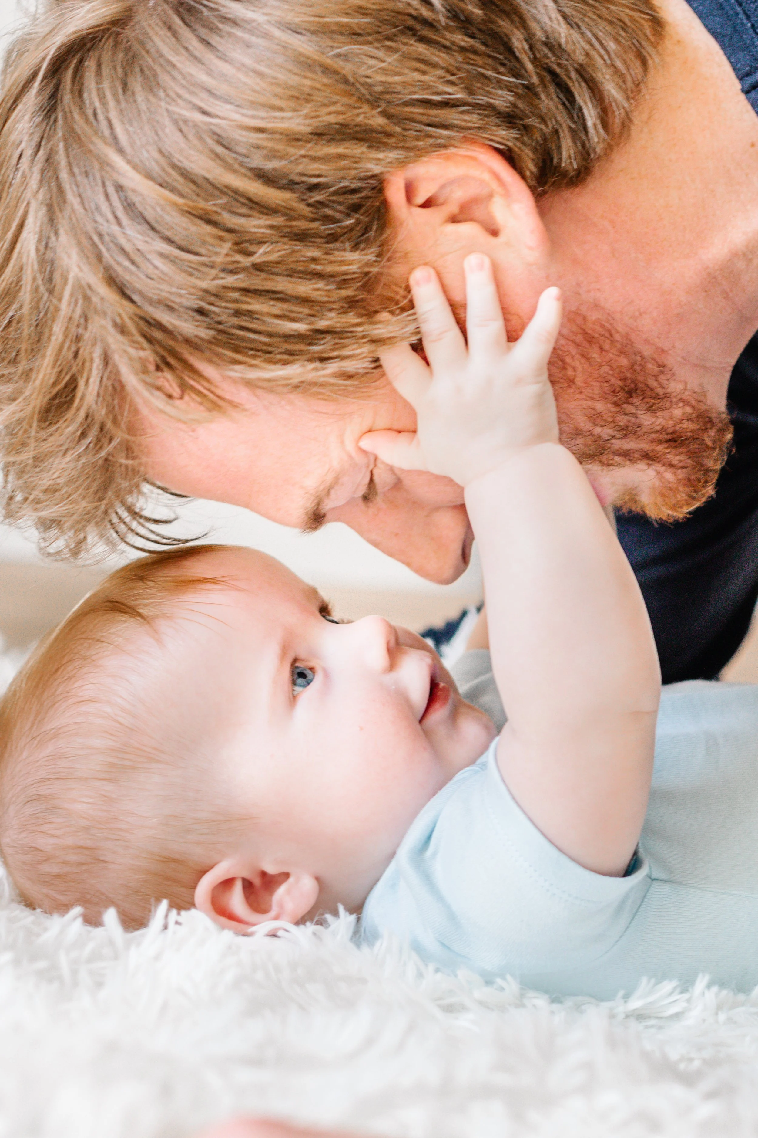 Baby touching a man's face on a soft surface.