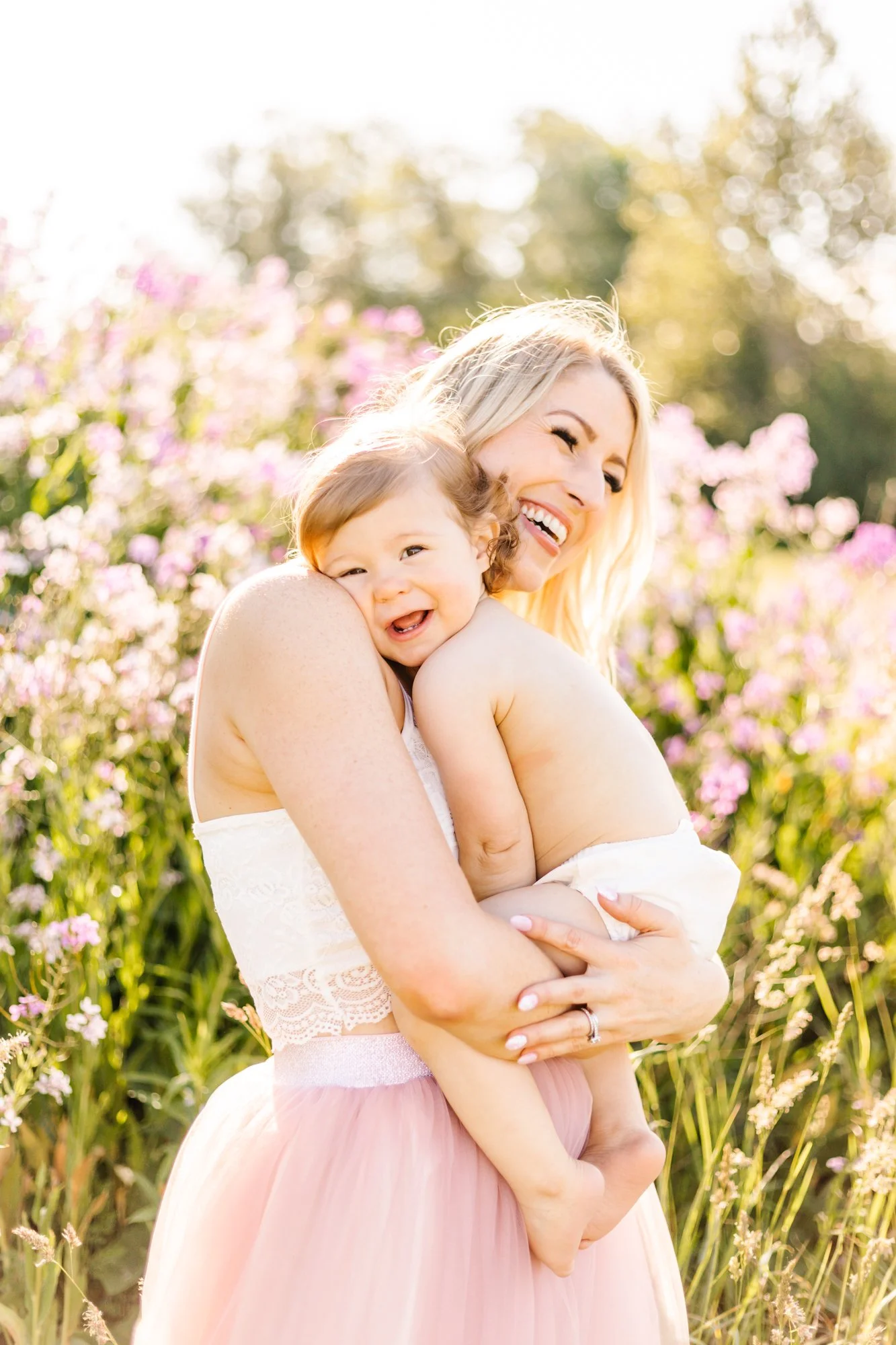 A joyful woman holding a laughing baby in a field of purple flowers.