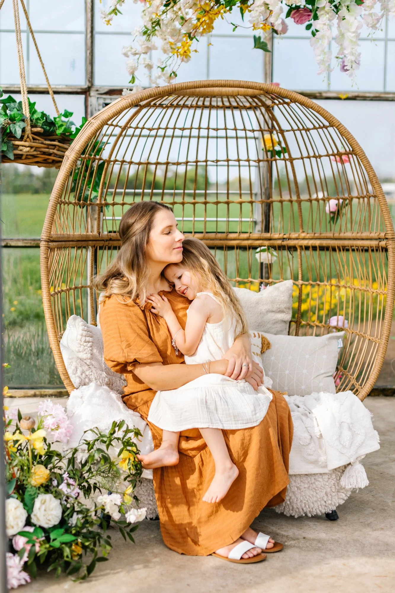 Mother and daughter cuddling on a wicker swing chair surrounded by flowers.
