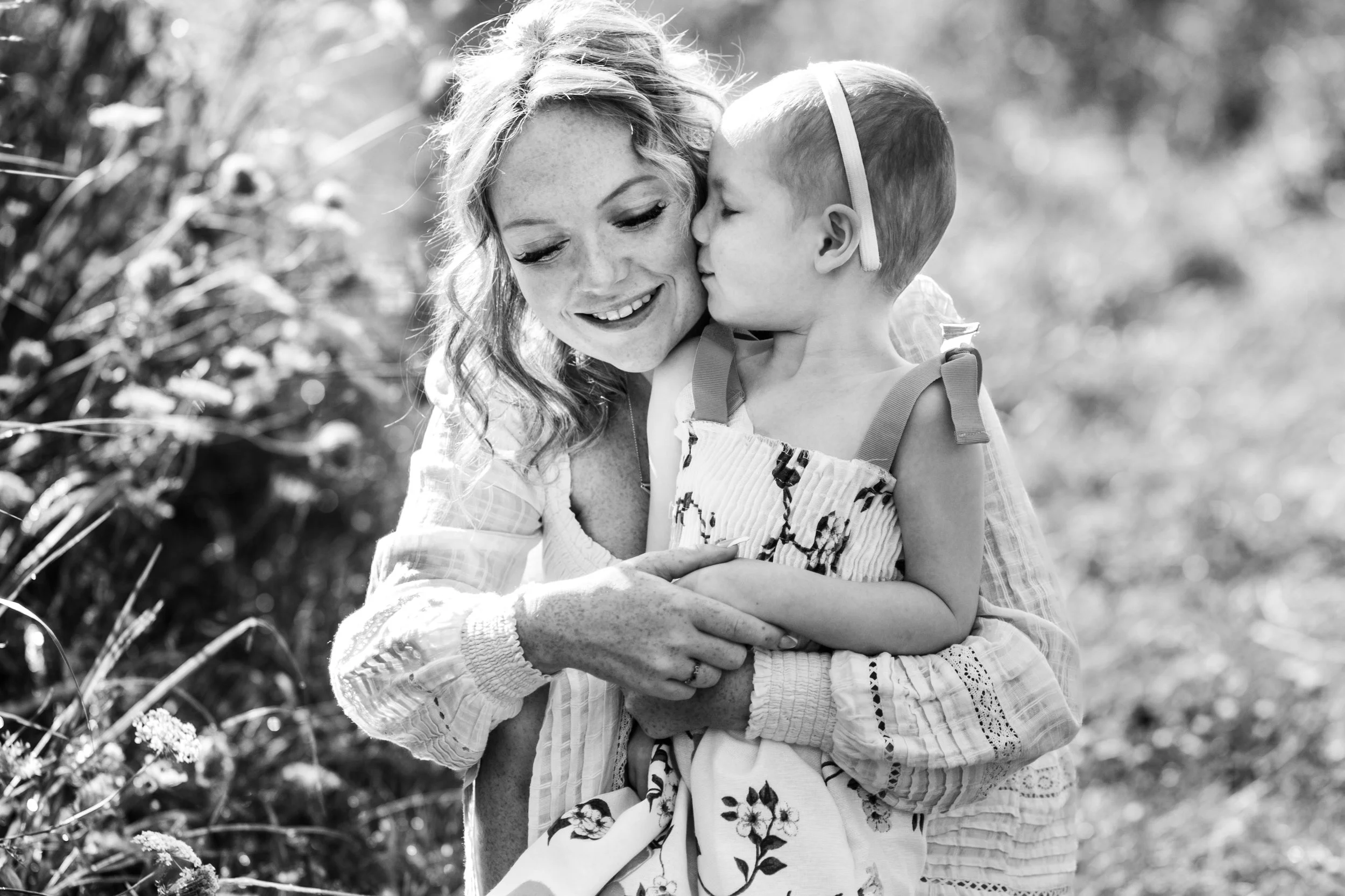 Black and white photo of a smiling woman cuddling a young child in a field.