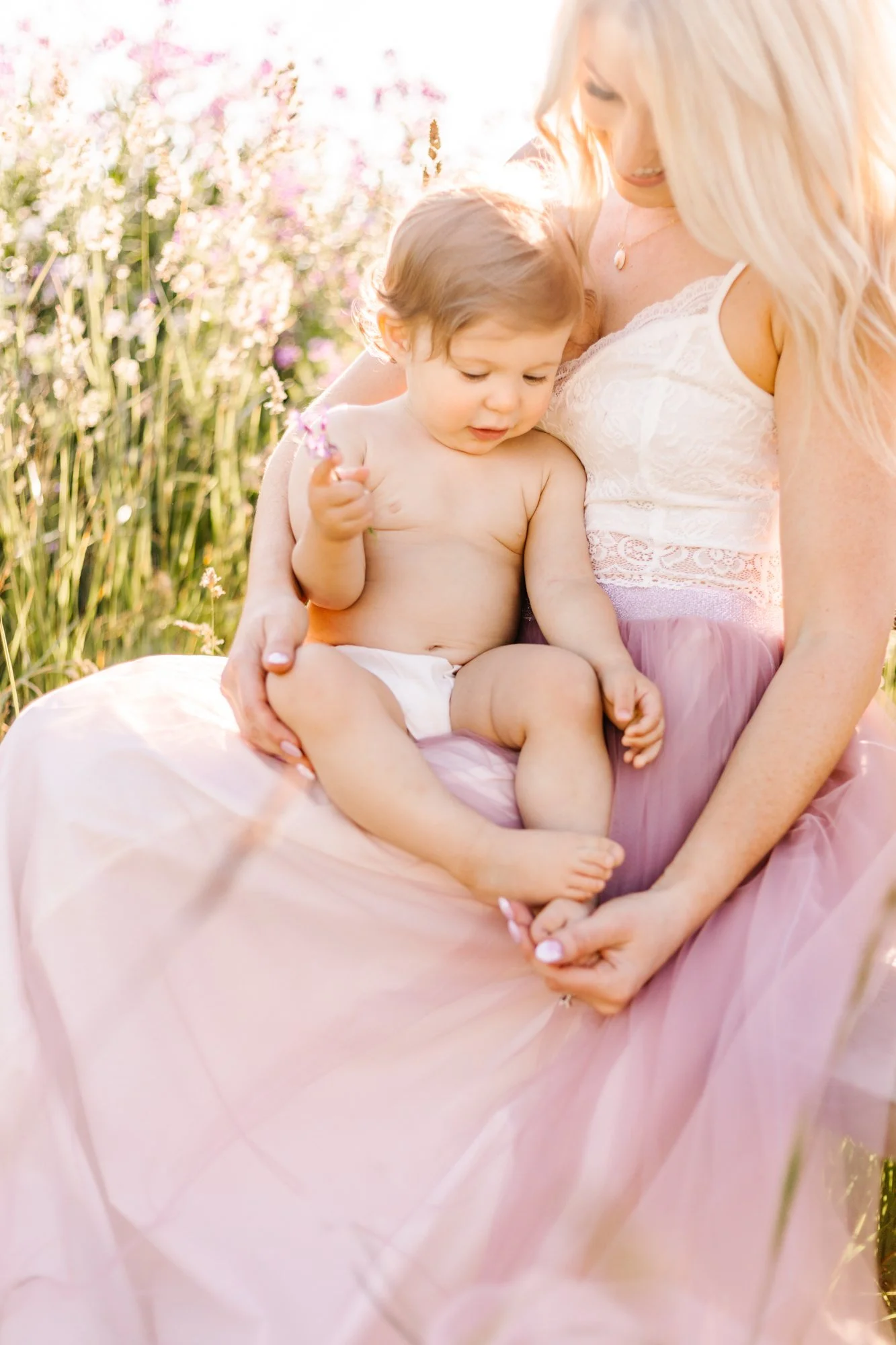 Woman in white lace top holding a baby outdoors in a field of flowers.
