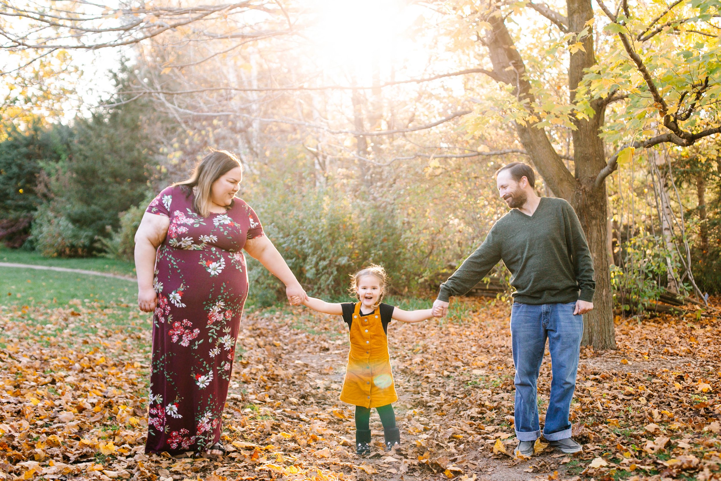 Family of three holding hands outdoors in a park with autumn leaves.