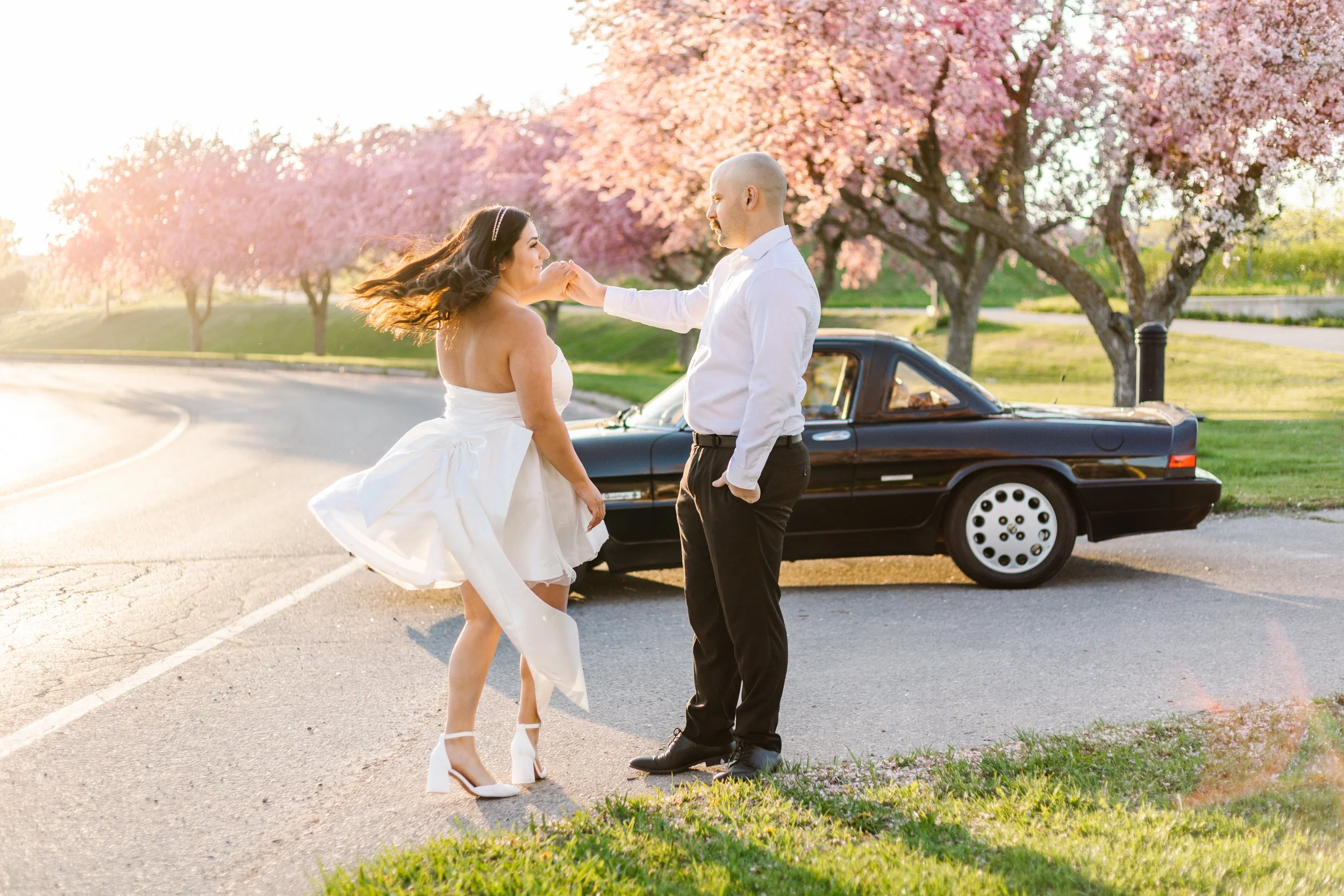 Couple dancing near a black convertible with cherry blossoms in the background.