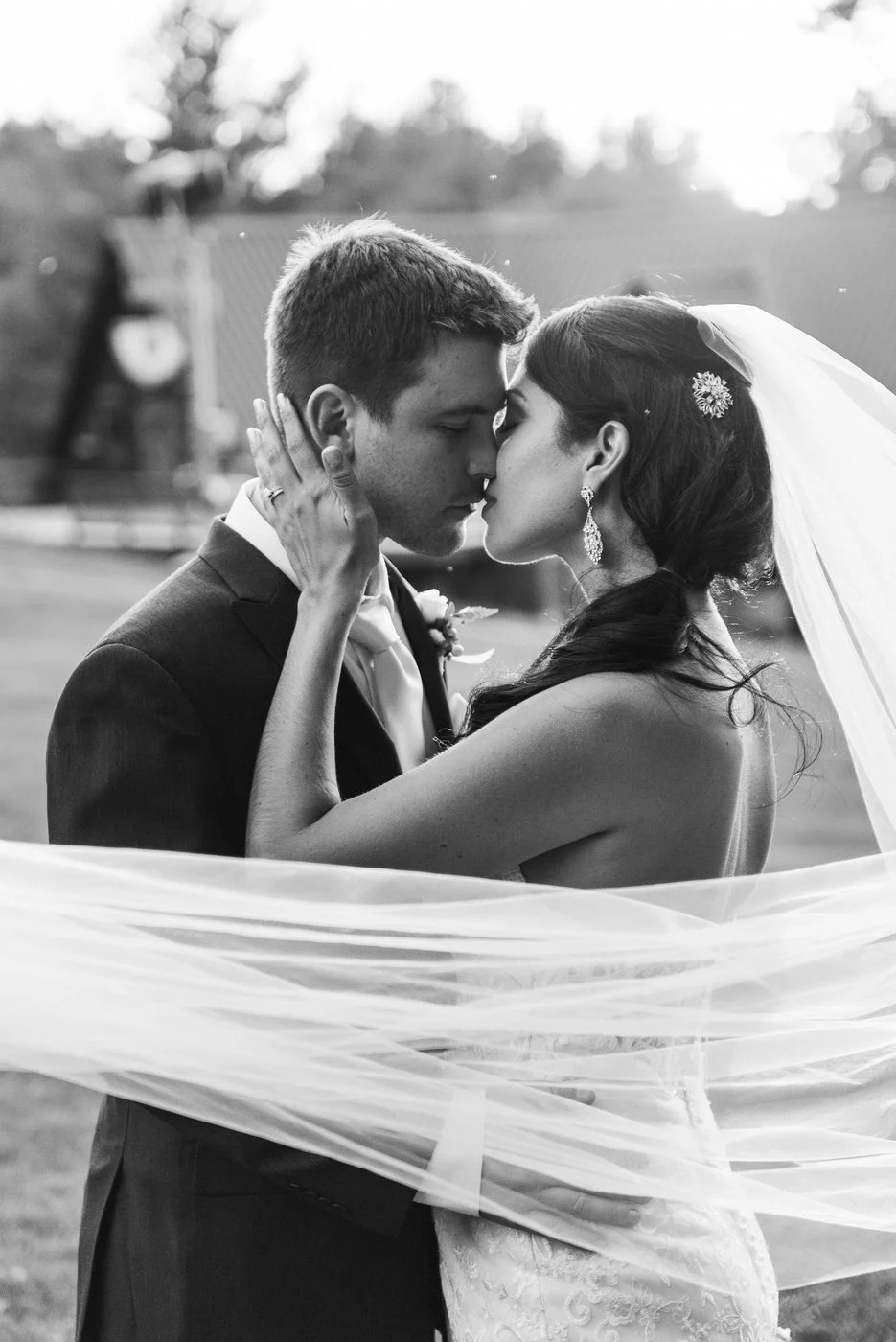 Bride and groom kissing, wrapped in veil, wedding moment, black and white photo.