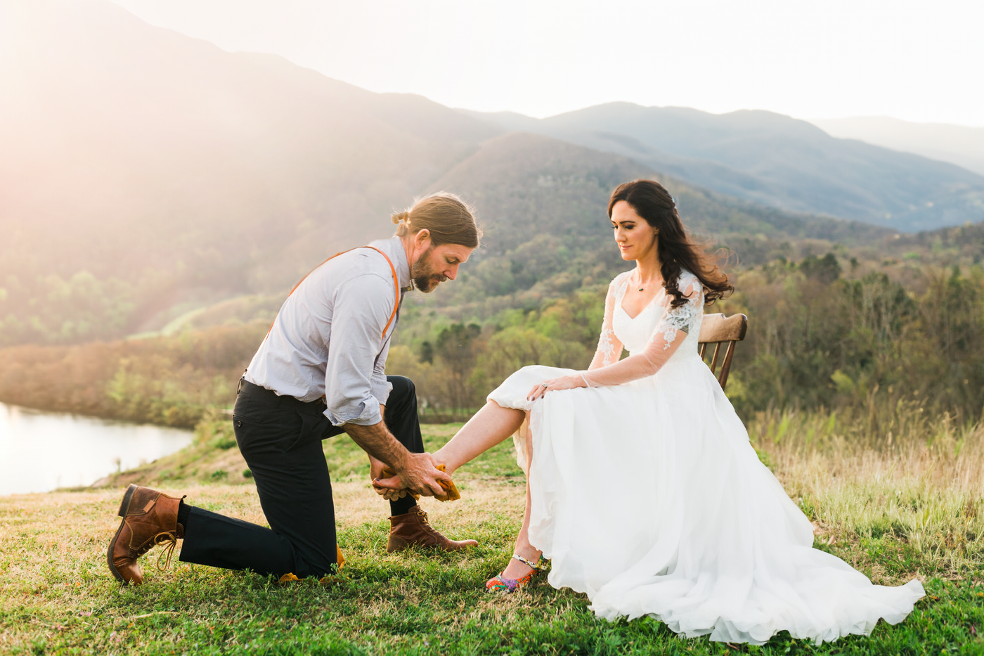 Man kneeling putting shoes on a woman in a wedding dress on a hill