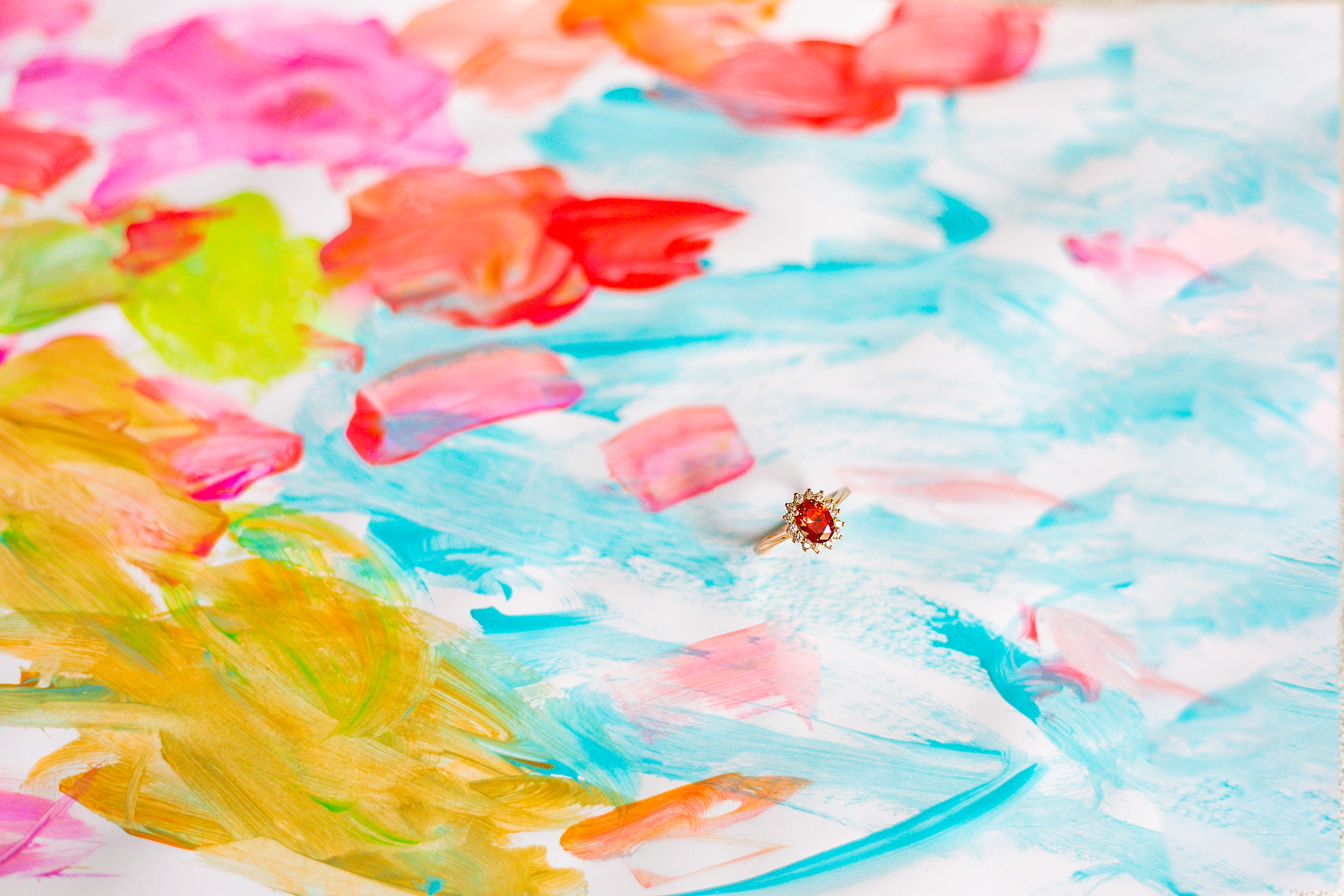 Colorful abstract painting with a gold ring featuring a red gemstone in the center.