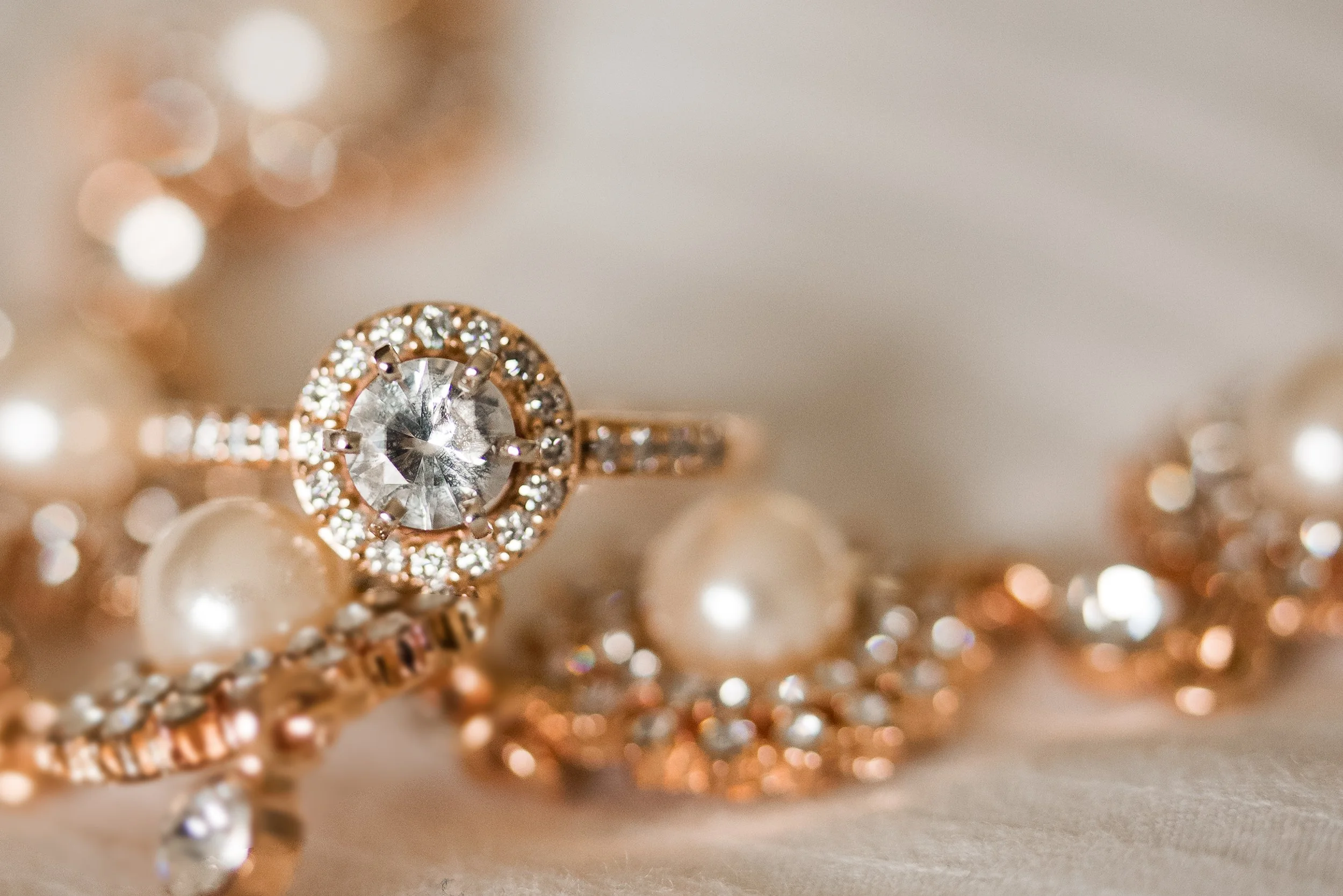 Close-up of a diamond engagement ring with a halo setting, surrounded by pearls and gold jewelry.