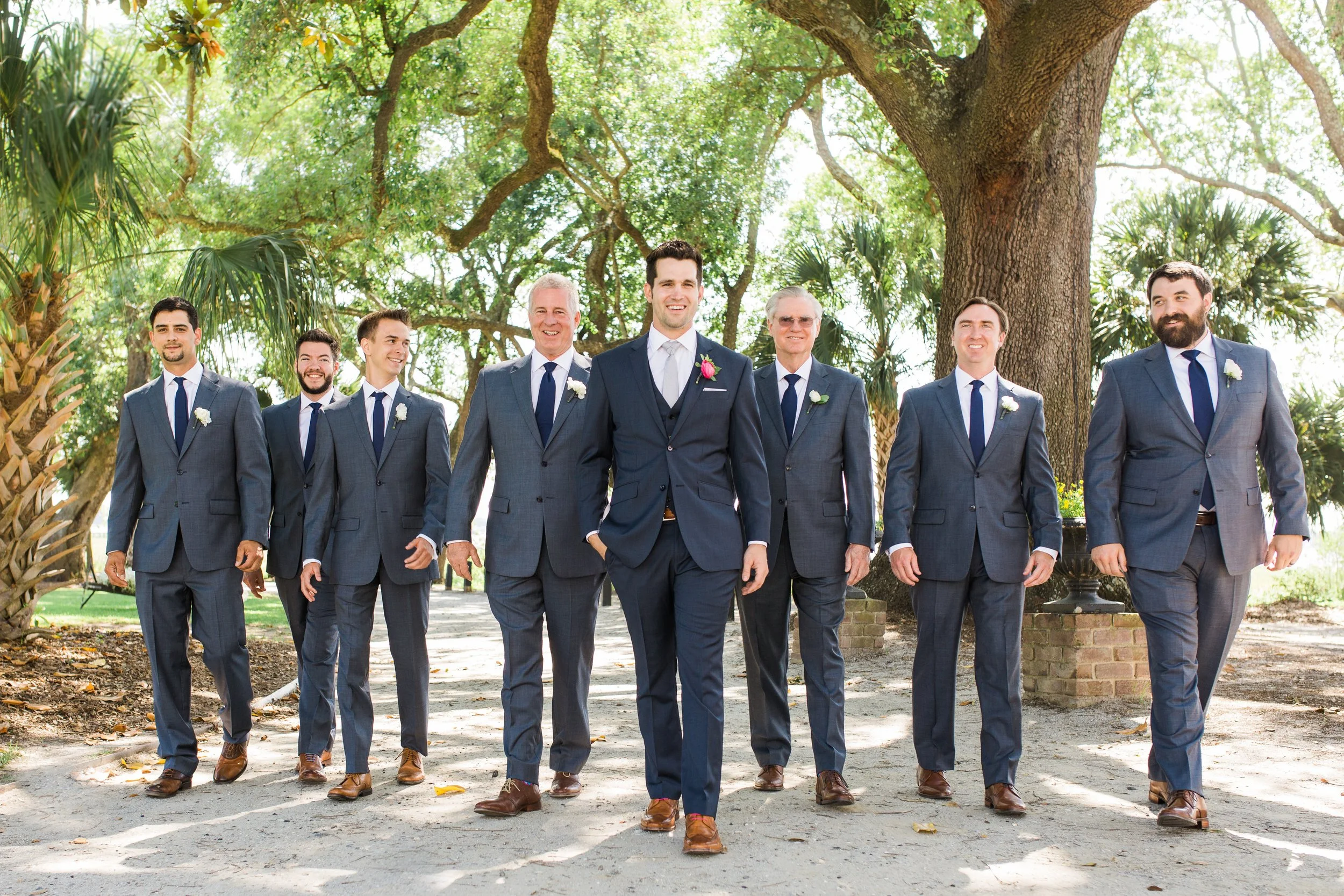Group of groomsmen in suits walking outdoors under trees