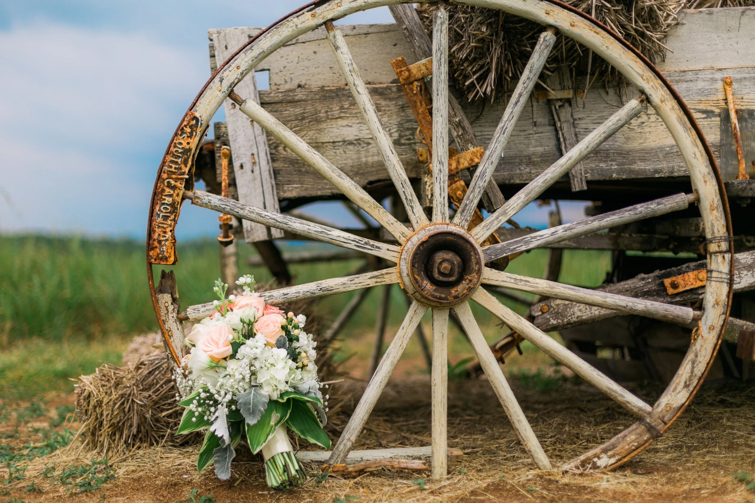 Rustic wooden wagon wheel with a bouquet of flowers laid against it in a field.