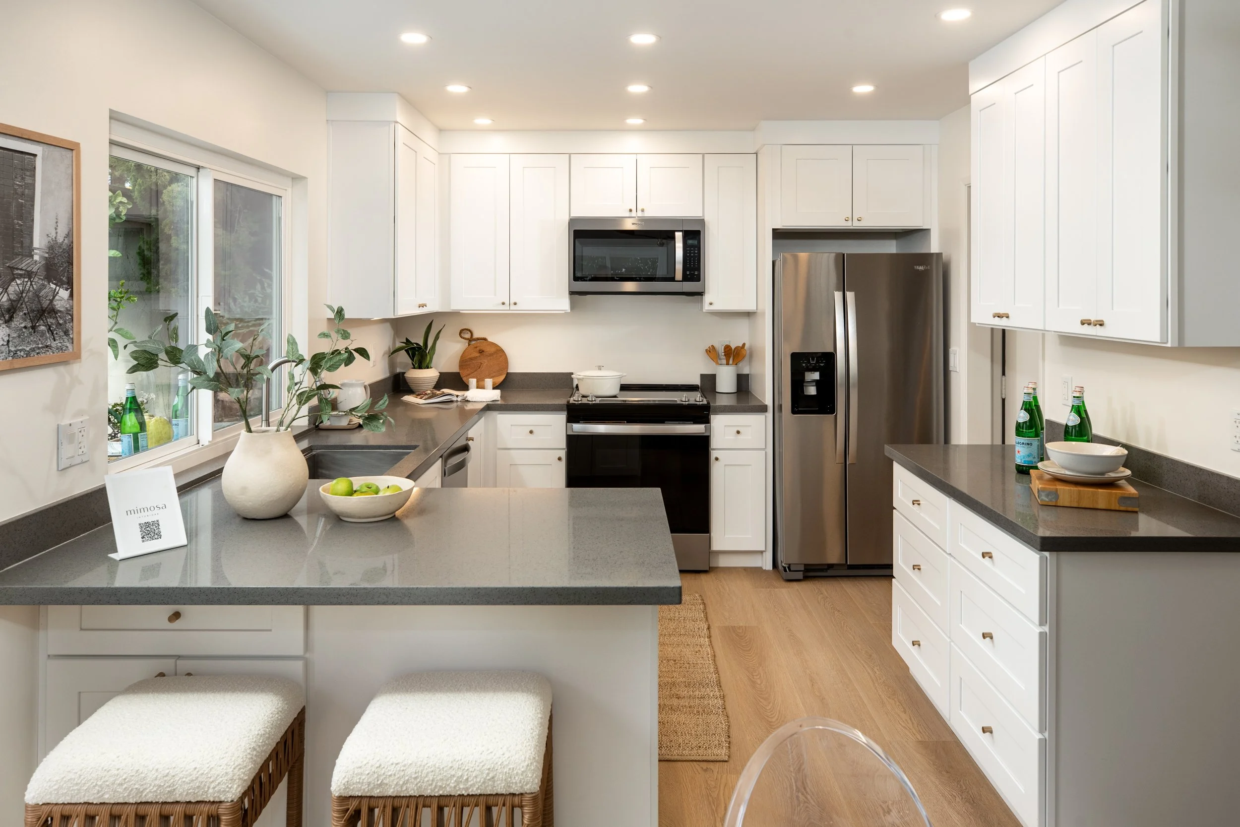 Modern kitchen with white cabinets, gray countertops, stainless steel appliances, and wood flooring.