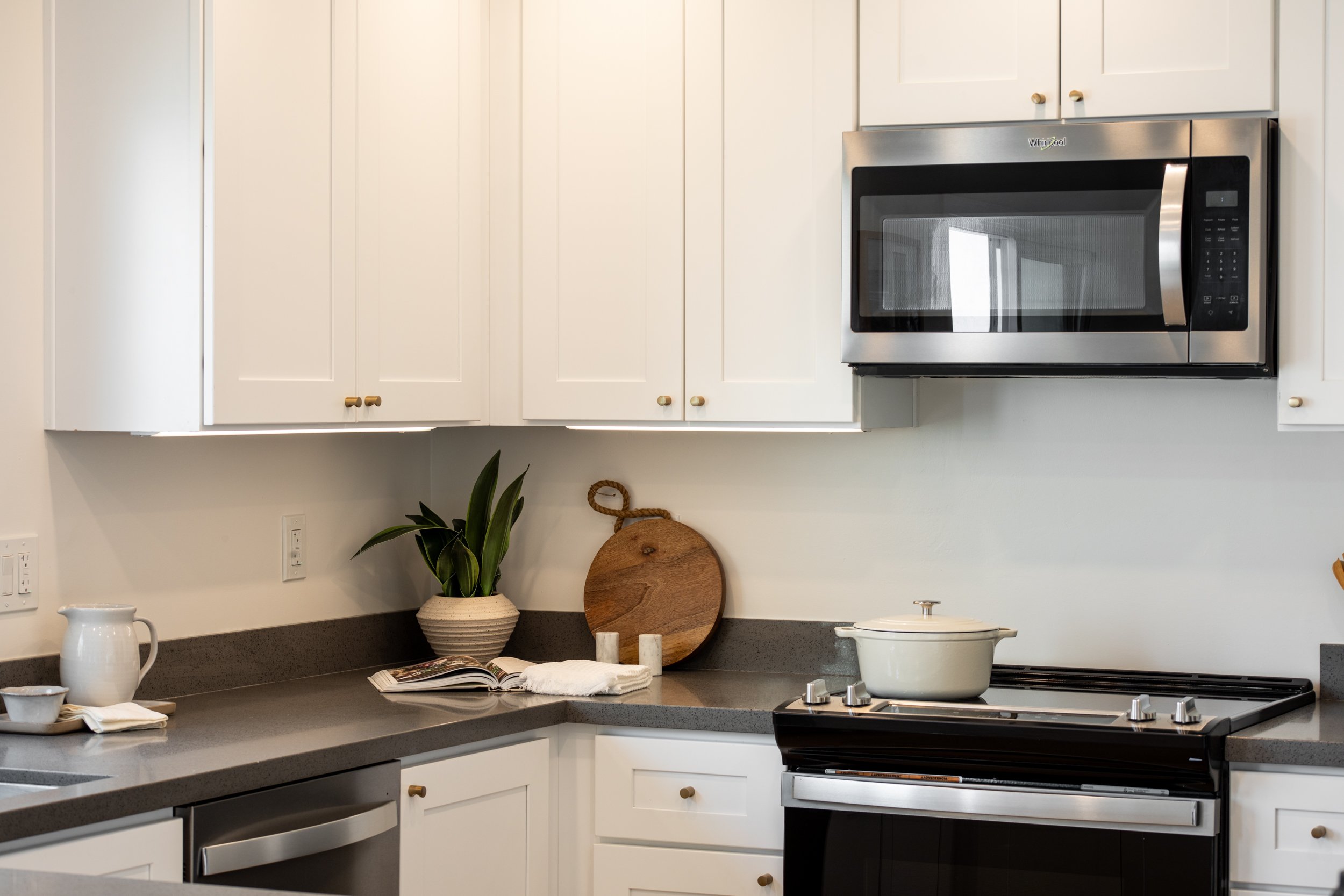 White kitchen with microwave, stove, and countertop with plants, cutting board, pitcher, and dishes.
