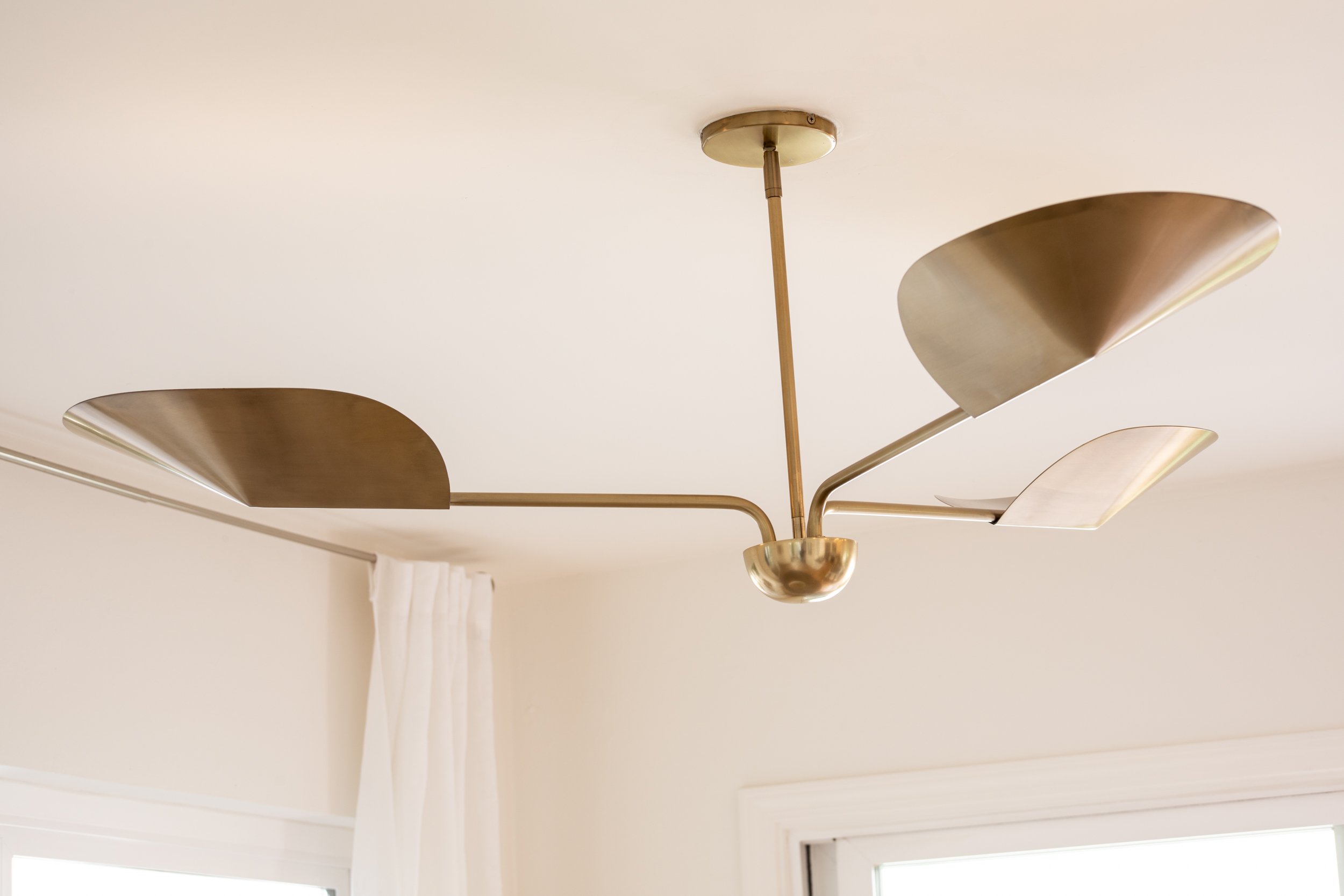 Modern chandelier with brass finish and curved arm design installed on a white ceiling.