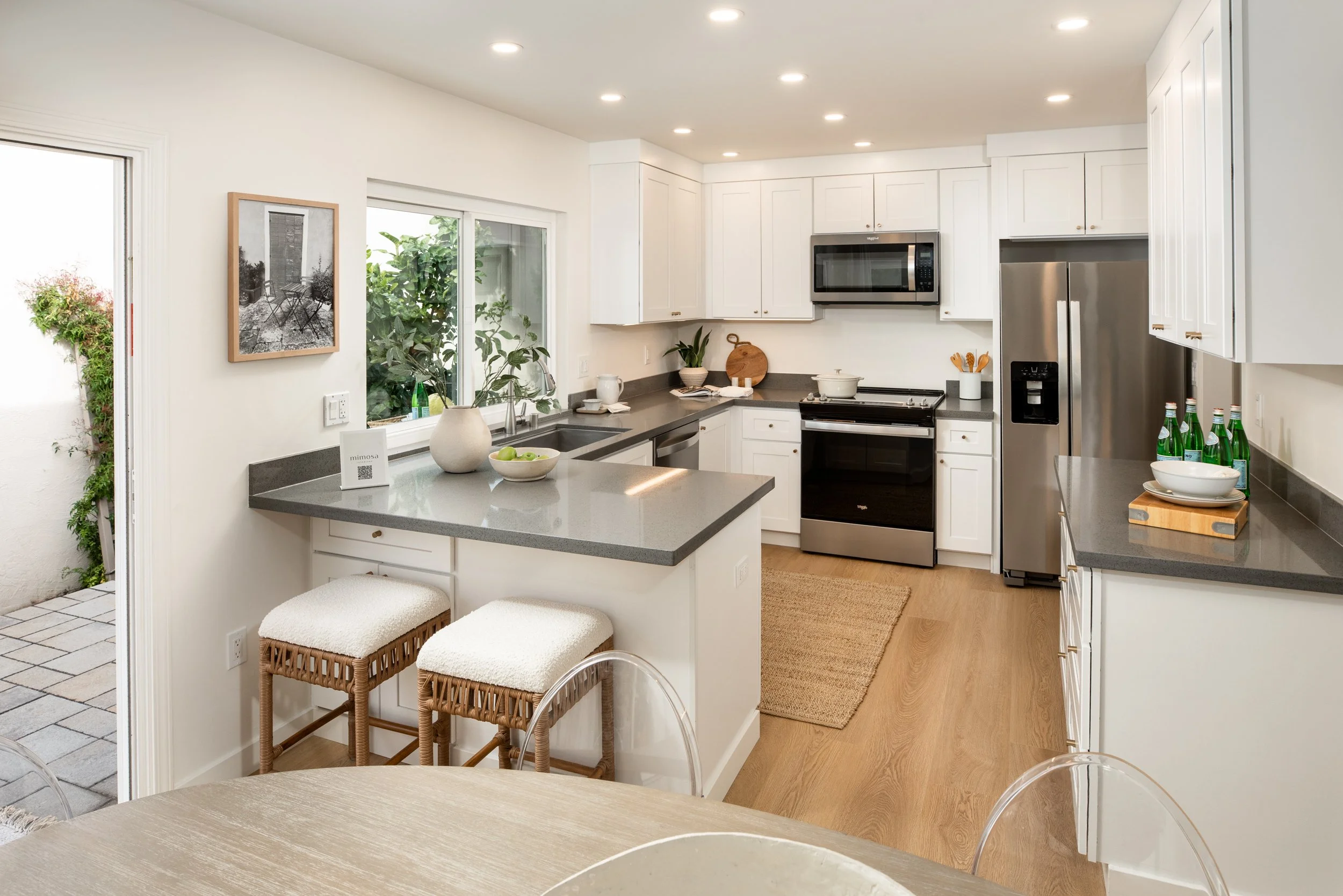 Modern kitchen with white cabinets, black countertops, stainless steel appliances, and hardwood floors.
