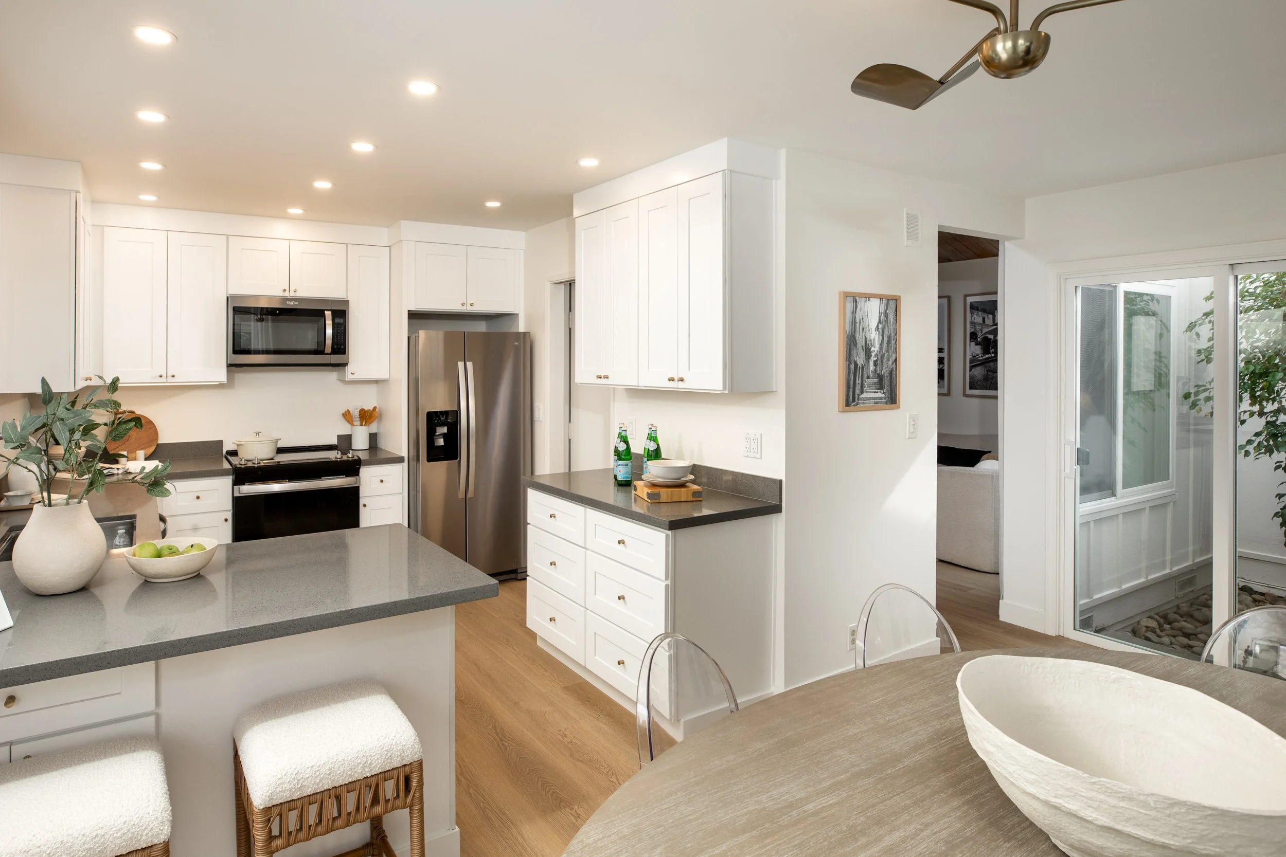 Bright modern kitchen with white cabinets, stainless steel refrigerator, black microwave, and countertop with dining table and chairs.