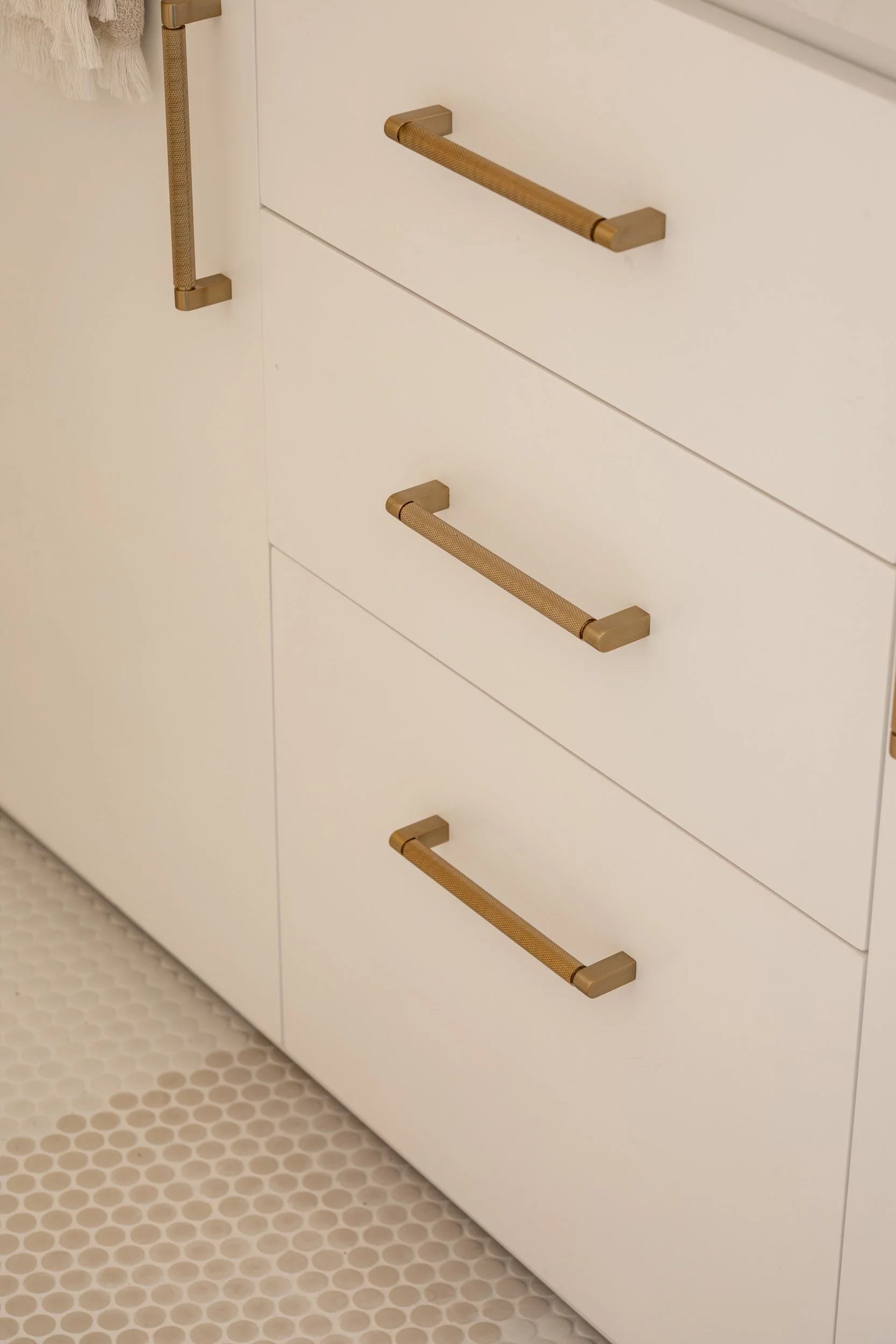 Close-up of a white cabinets with three gold-colored handles, situated on a light-colored tiled floor.