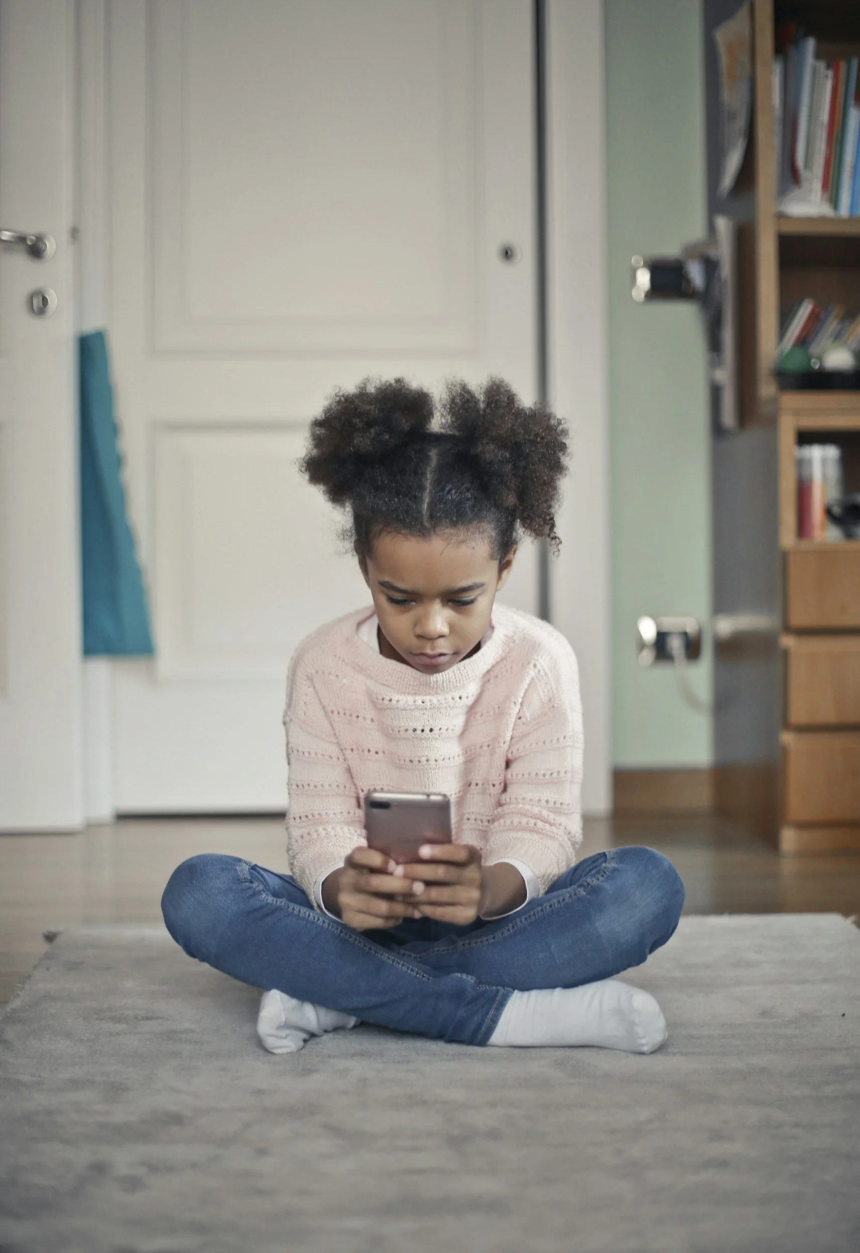 Child sitting alone on the floor using a smartphone, representing children's everyday use of apps and games
